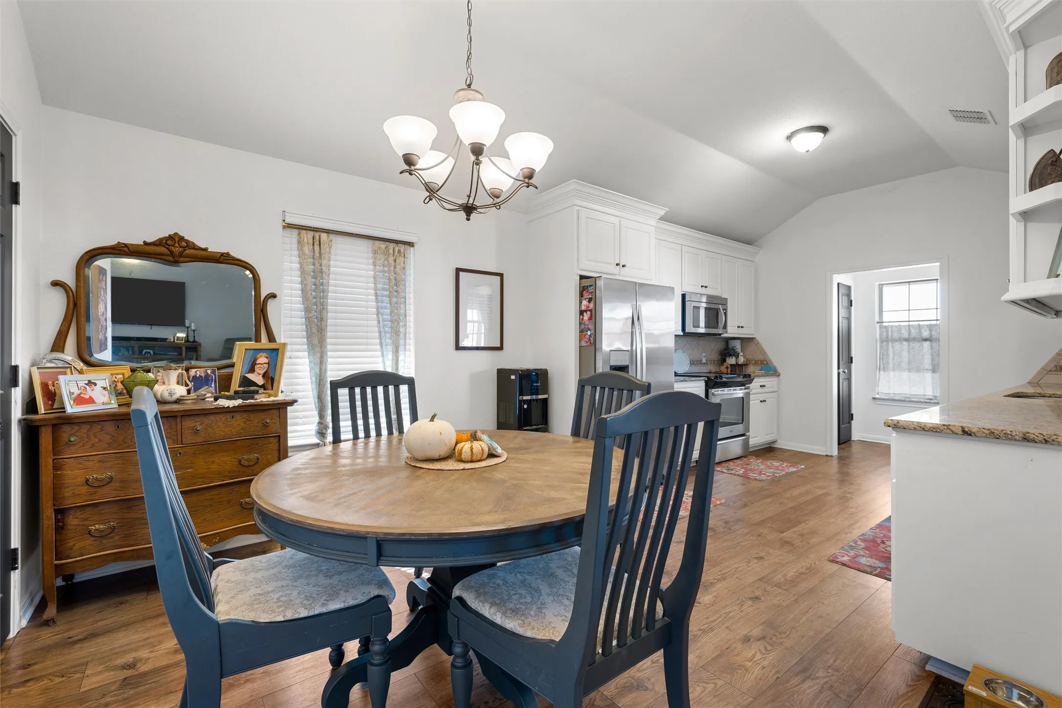 Vaulted ceiling, wood-finish flooring, white cabinetry, stainless steel appliances, and a built-in kitchen peninsula with a stone countertop