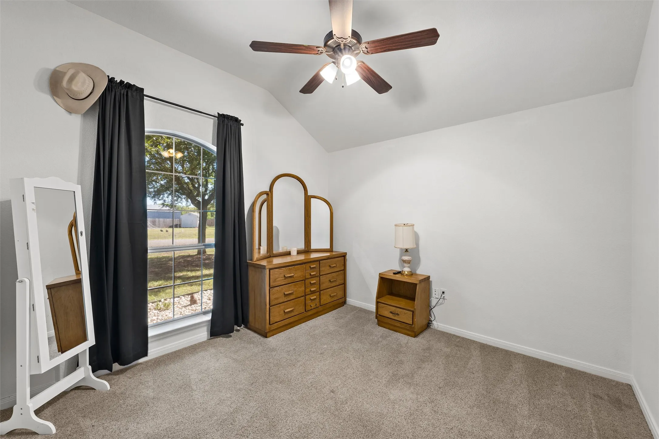 Vaulted ceiling featuring a ceiling fan with integrated lighting, arched window, and carpeted flooring