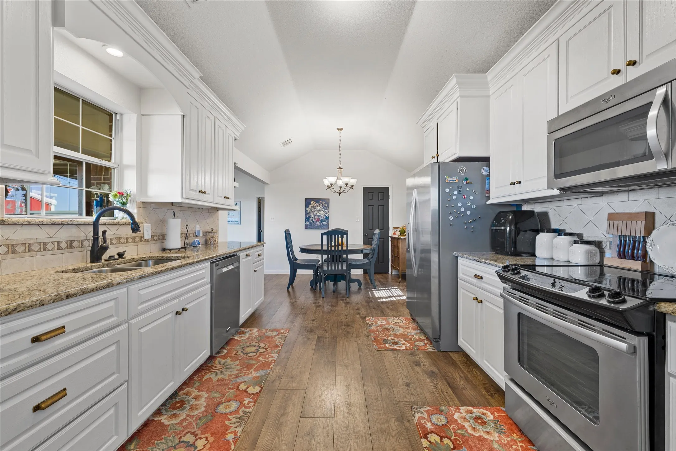 Kitchen featuring white cabinetry, granite countertops, stainless steel appliances, wood-finish flooring, and a vaulted ceiling