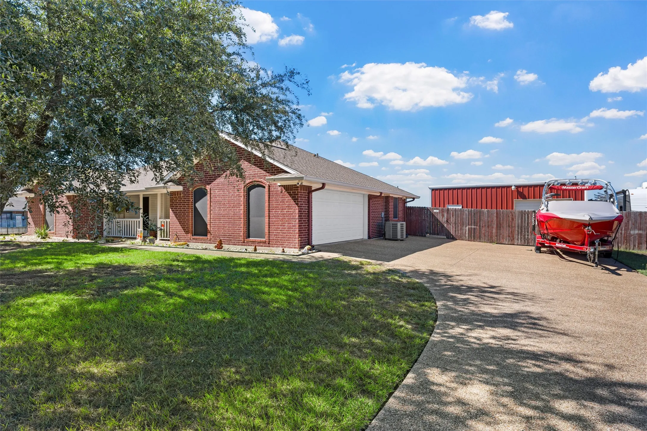 Brick exterior, arched windows, covered front porch with white railing, attached garage, and paved driveway