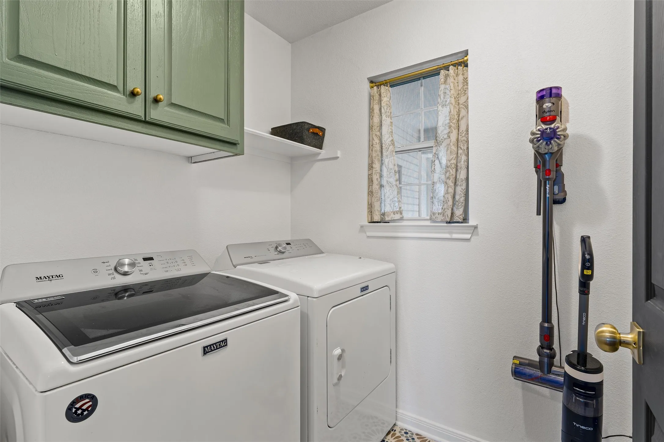Built-in cabinetry with gold-toned hardware, white wall shelving, and a window with trim
