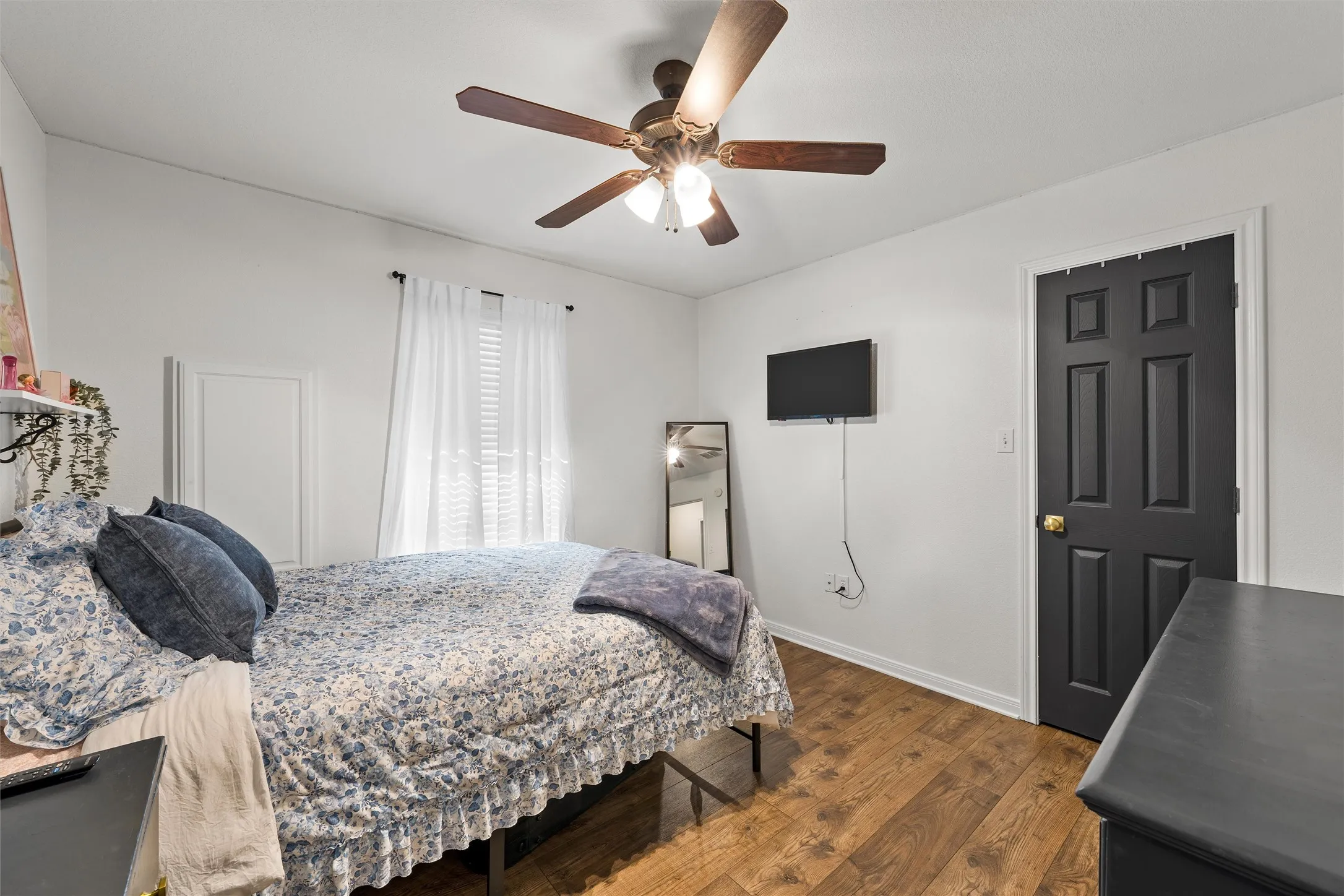 Wood-finish flooring, ceiling fan with integrated lighting, window with blinds, and a paneled door