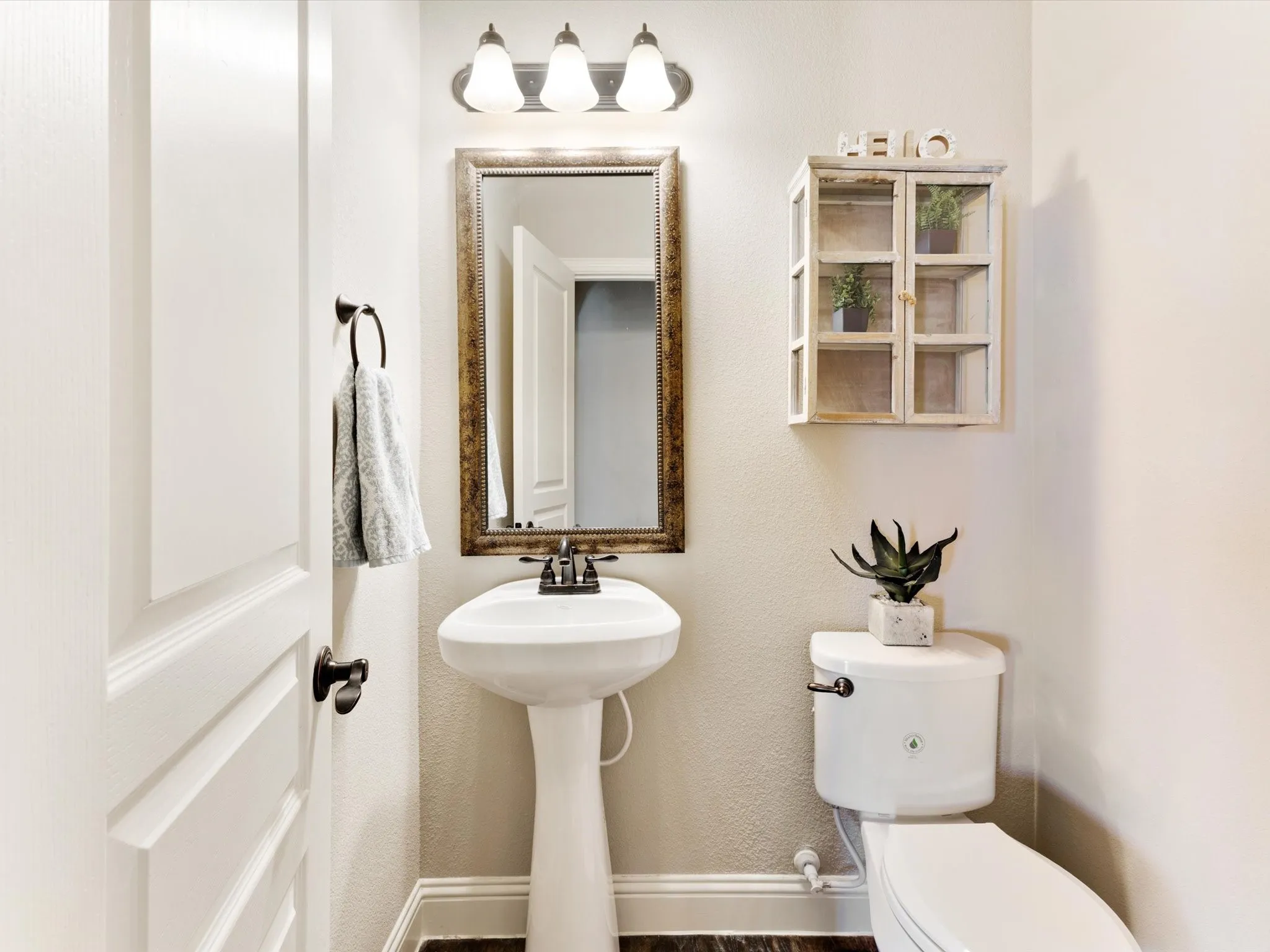 Pedestal sink, wall-mounted mirror with an ornate frame, and a three-light vanity fixture