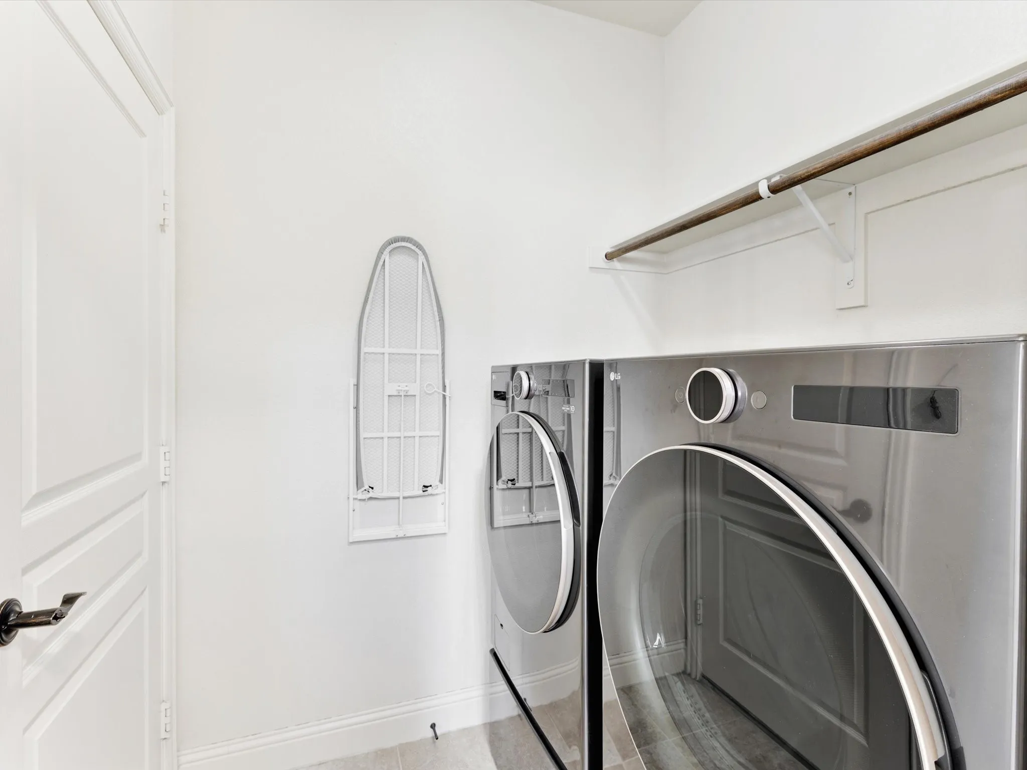 Dedicated laundry area with modern appliances, integrated shelving, and a wall-mounted ironing board