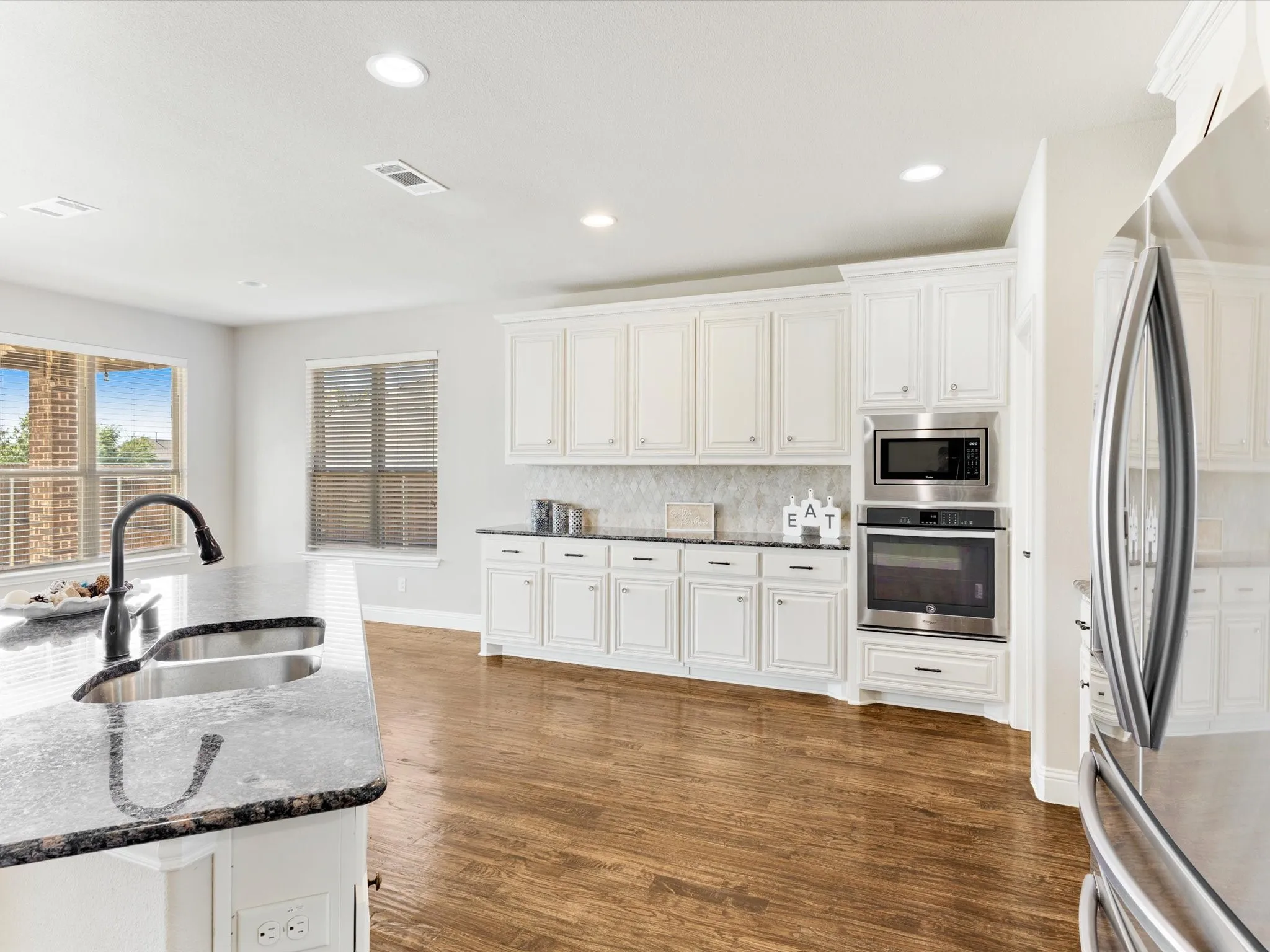 Kitchen featuring white cabinetry, dark stone countertops, stainless steel appliances, wood-finish flooring, and recessed lighting