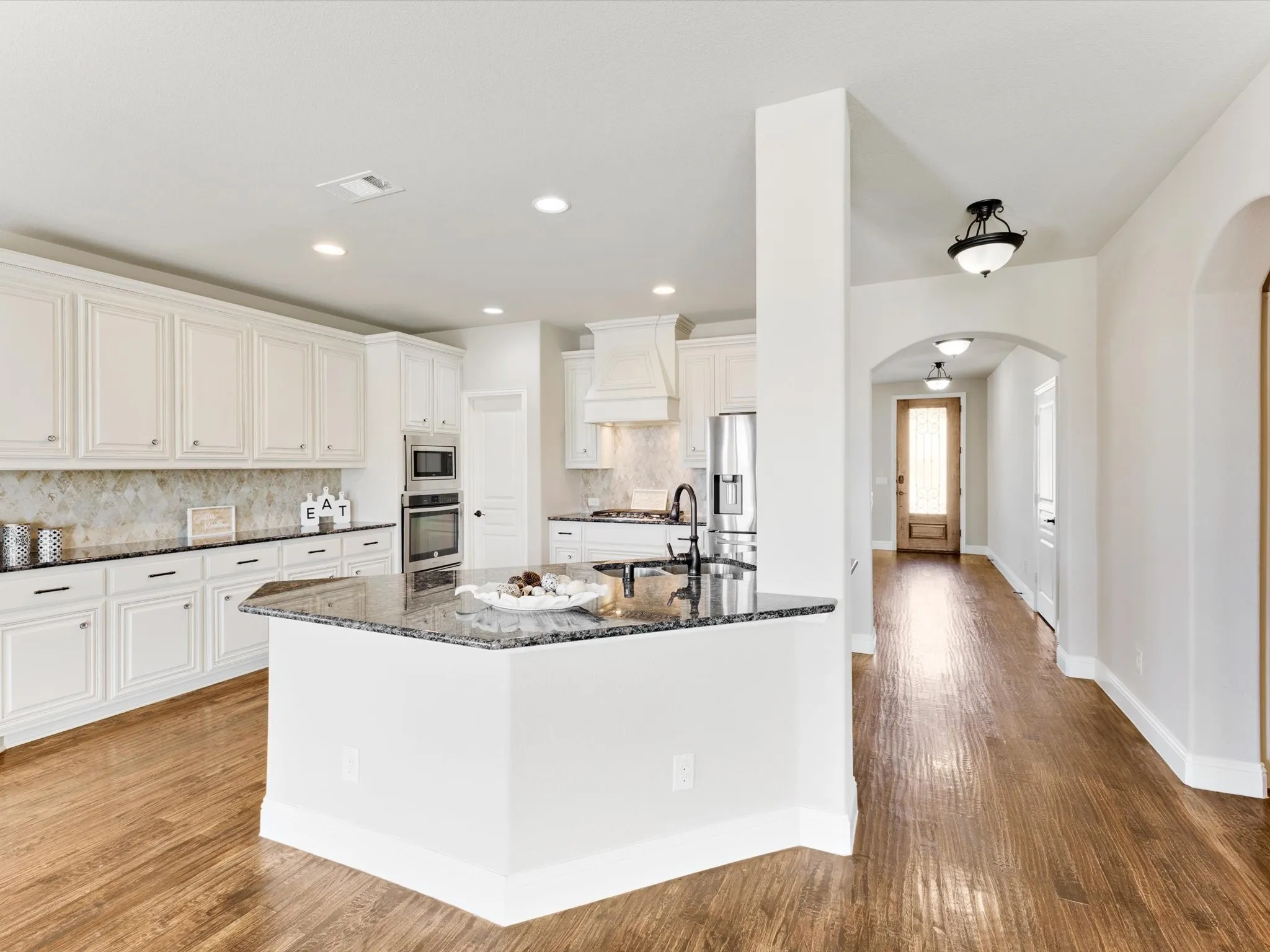 Kitchen featuring white cabinetry, dark stone countertops, an integrated stainless steel oven, and wood-finish flooring