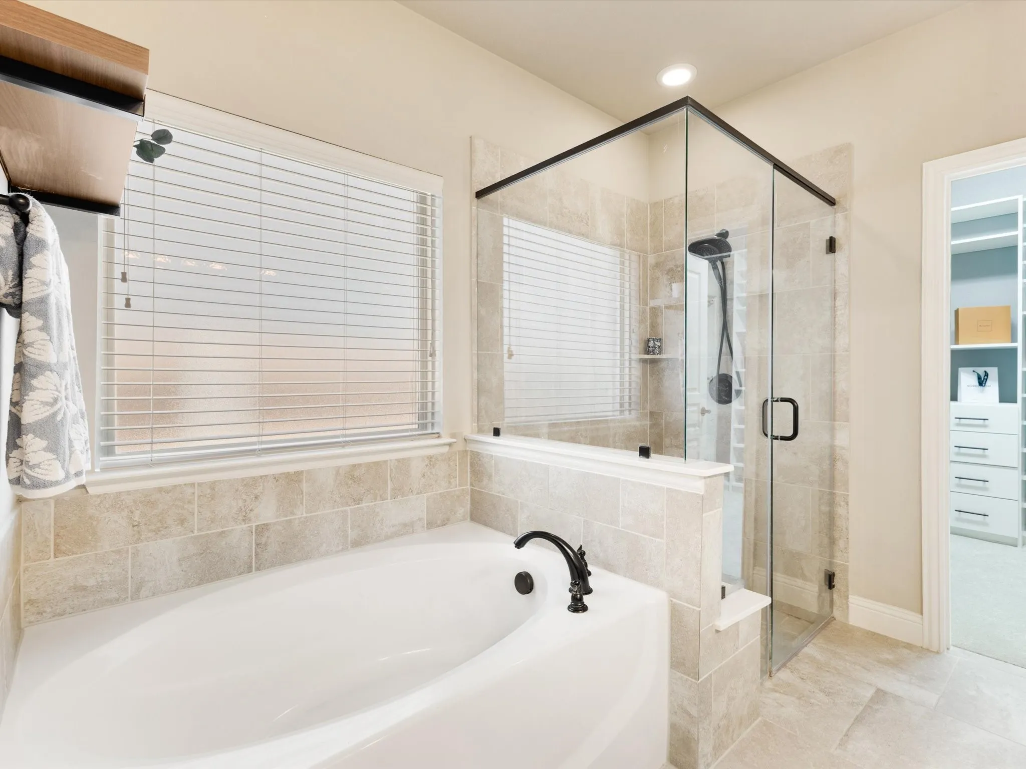 Built-in soaking tub with a black arch faucet, glass-enclosed shower with black hardware, and tiled walls and flooring