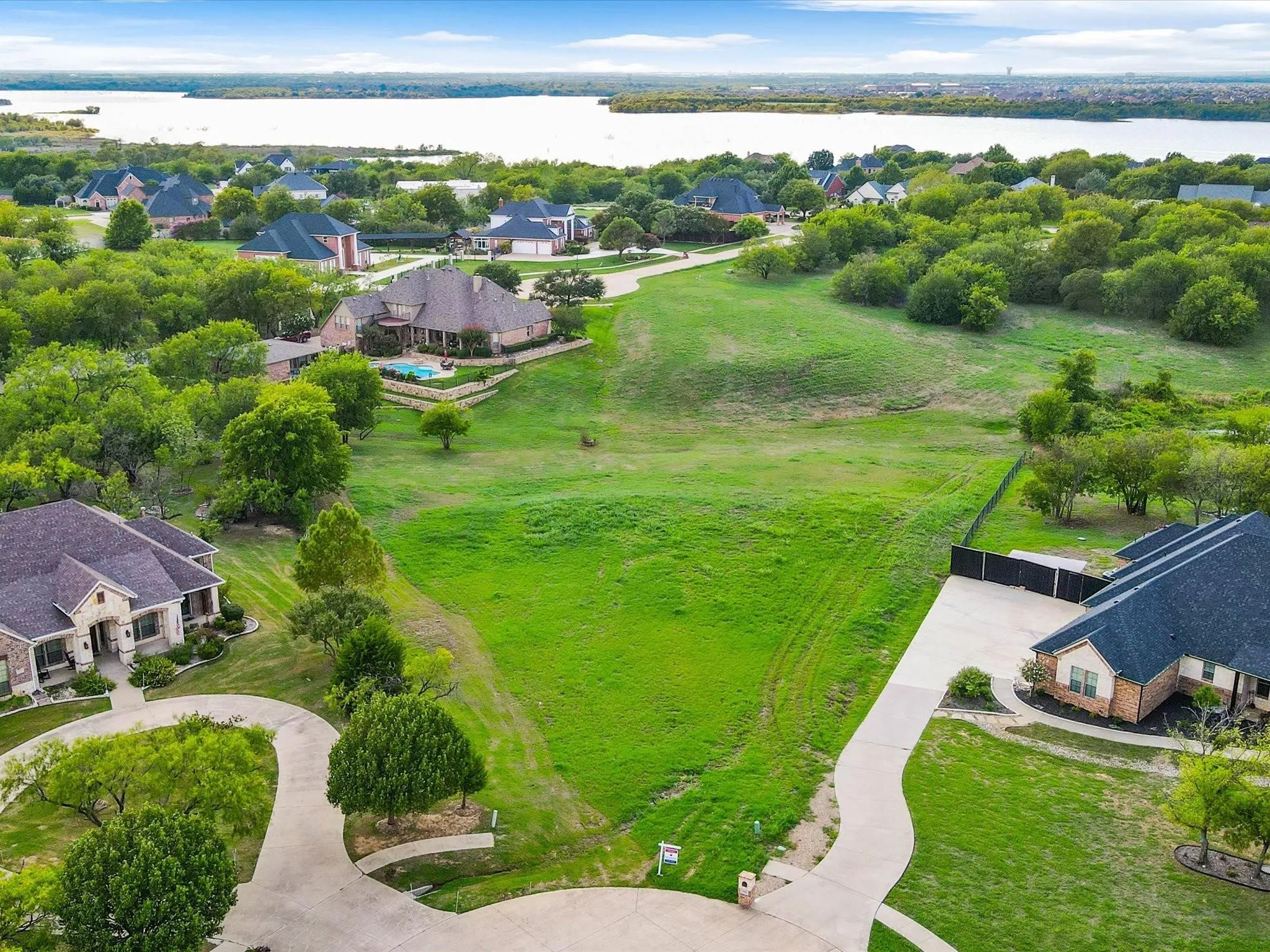 Expansive undeveloped lot with a gently sloping terrain, surrounded by mature trees, and featuring a concrete driveway