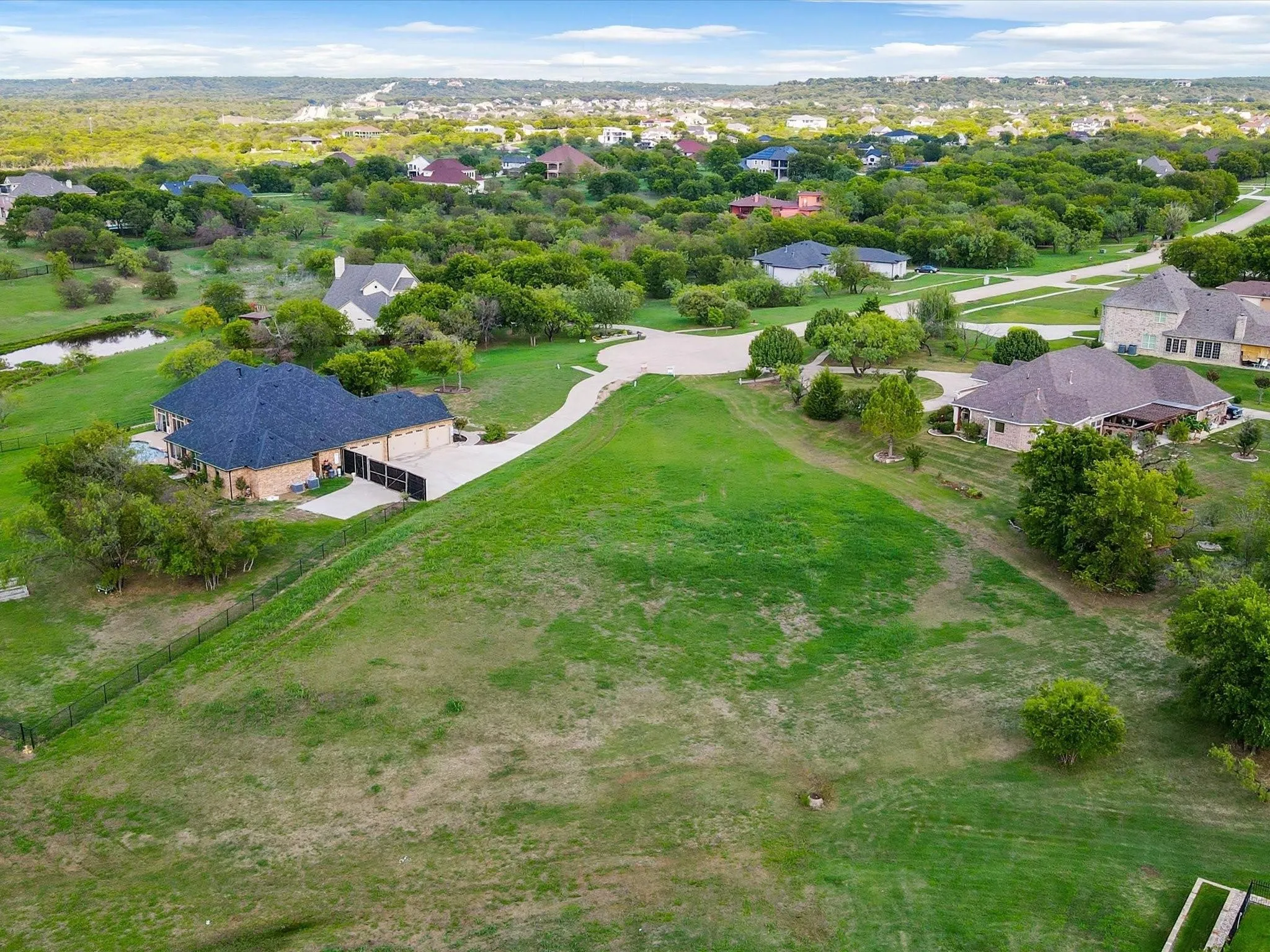 Expansive green space with distant residential properties, mature trees, and a small pond