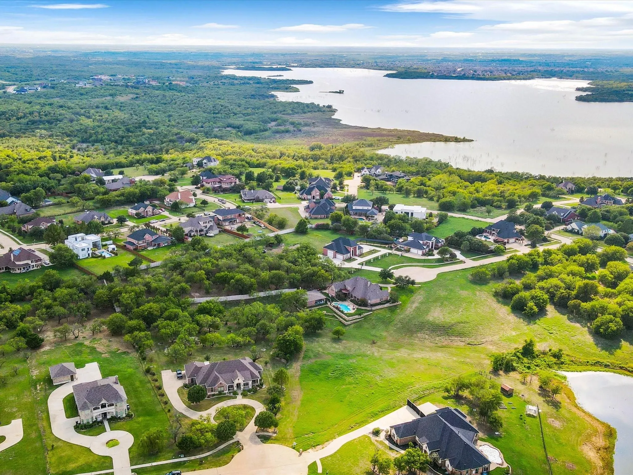 Expansive residential area featuring numerous properties, dense tree coverage, a large body of water, and some properties with private pools