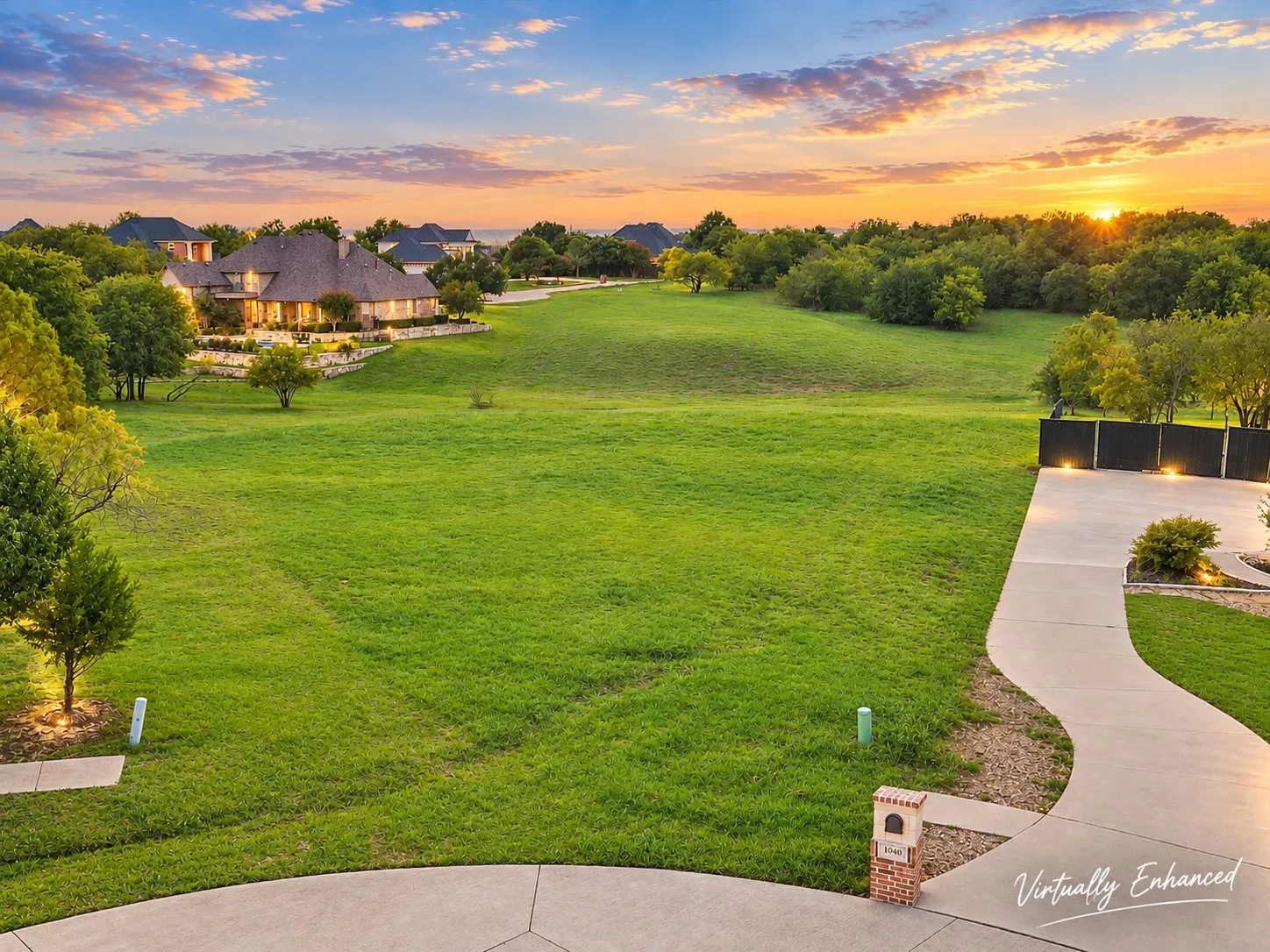 Expansive green space and a concrete driveway leading to a dark privacy fence with integrated lighting