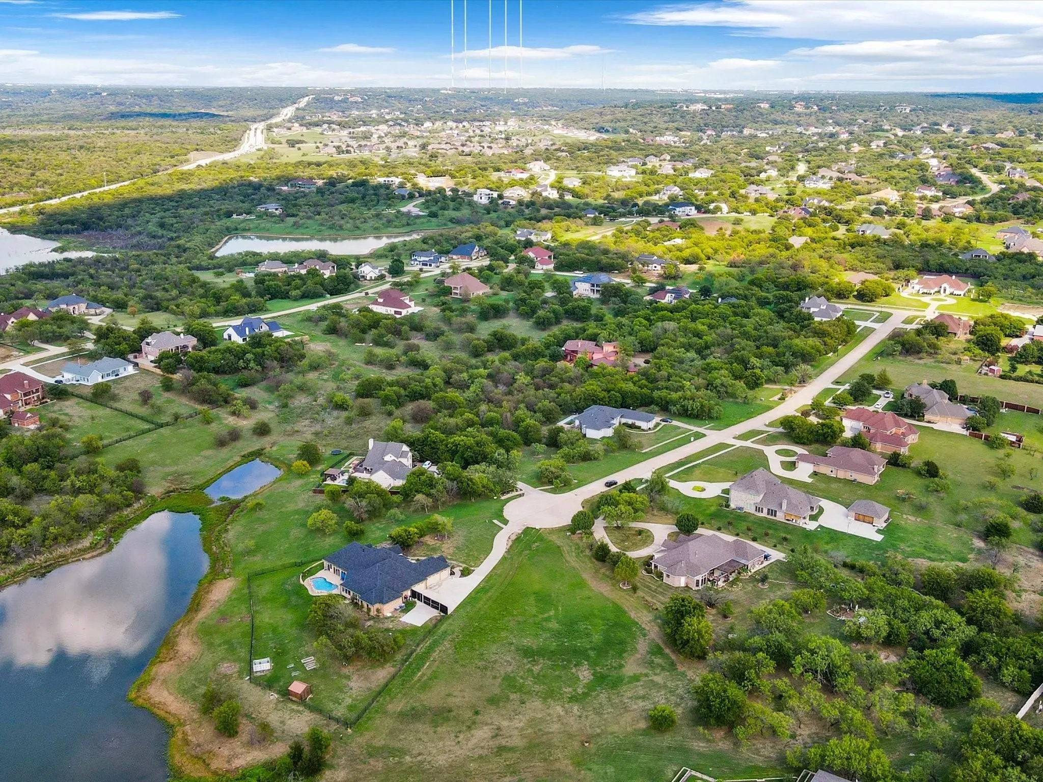 Expansive residential area featuring numerous properties, surrounding natural landscape, visible bodies of water, and a prominent road system