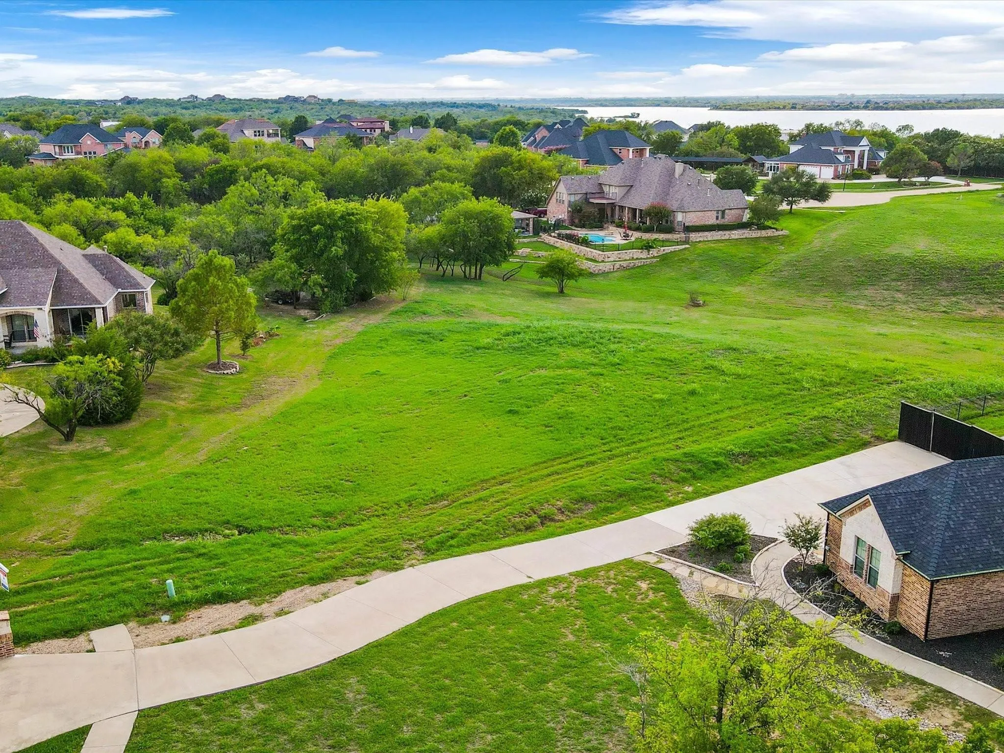 Expansive green land with a paved driveway and distant water body