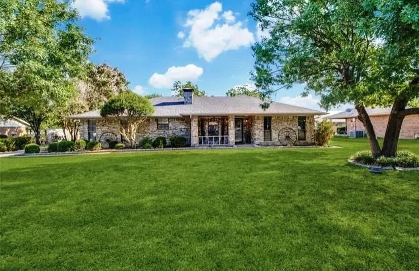 Stone exterior with a covered porch, mature trees, and a spacious lawn