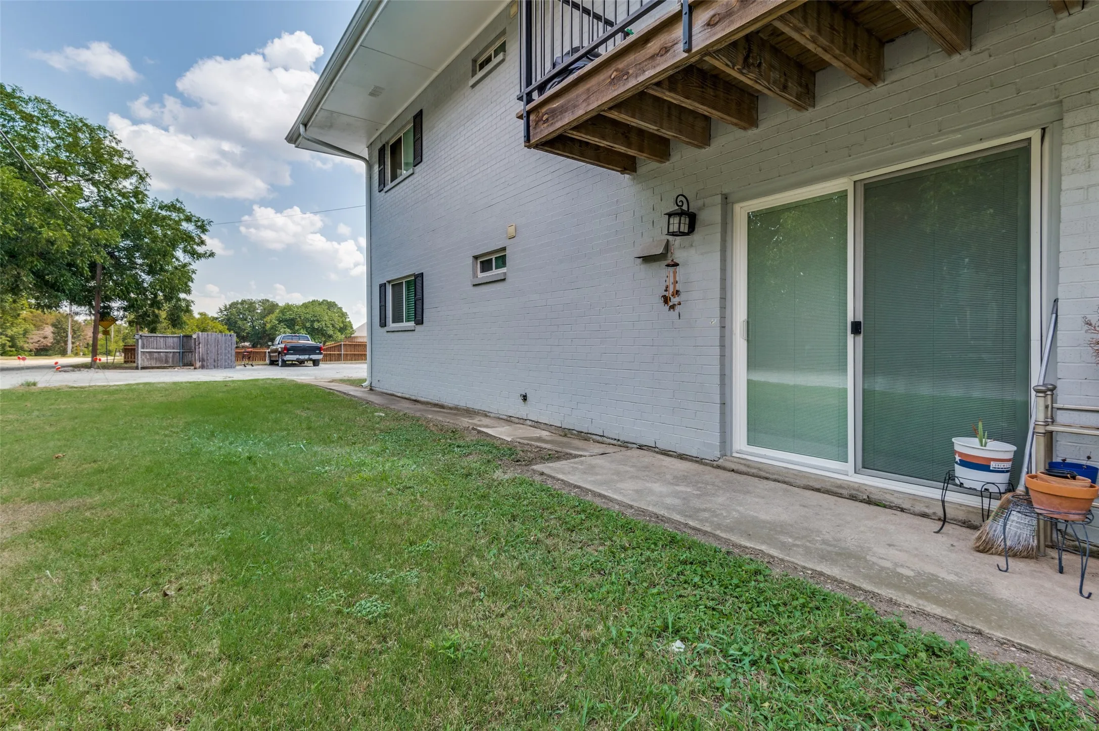 Ground-level patio with sliding glass door entry, exterior wall lantern, and mature landscaping