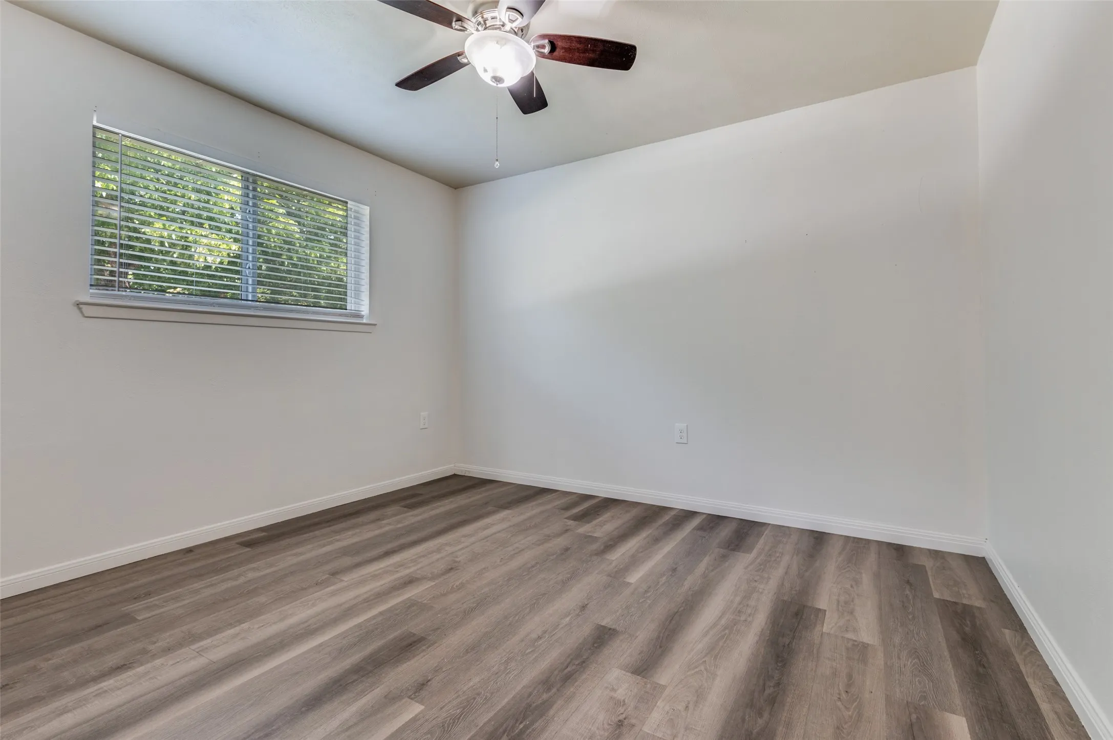 Wood-finish flooring, white walls, window with blinds, and a ceiling fan with integrated lighting