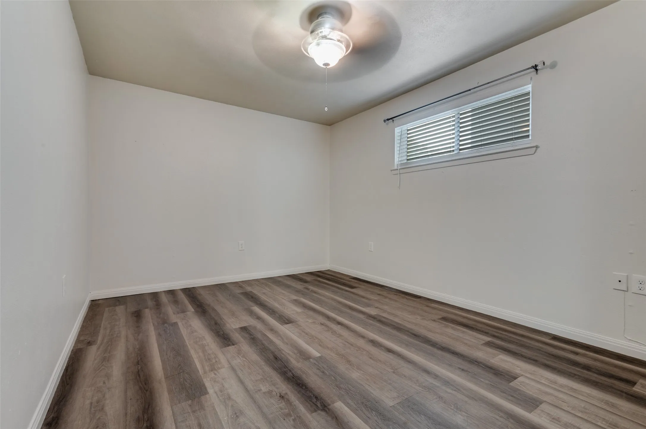 Wood-finish flooring, white walls, window with horizontal blinds, overhead ceiling light fixture, and white trim