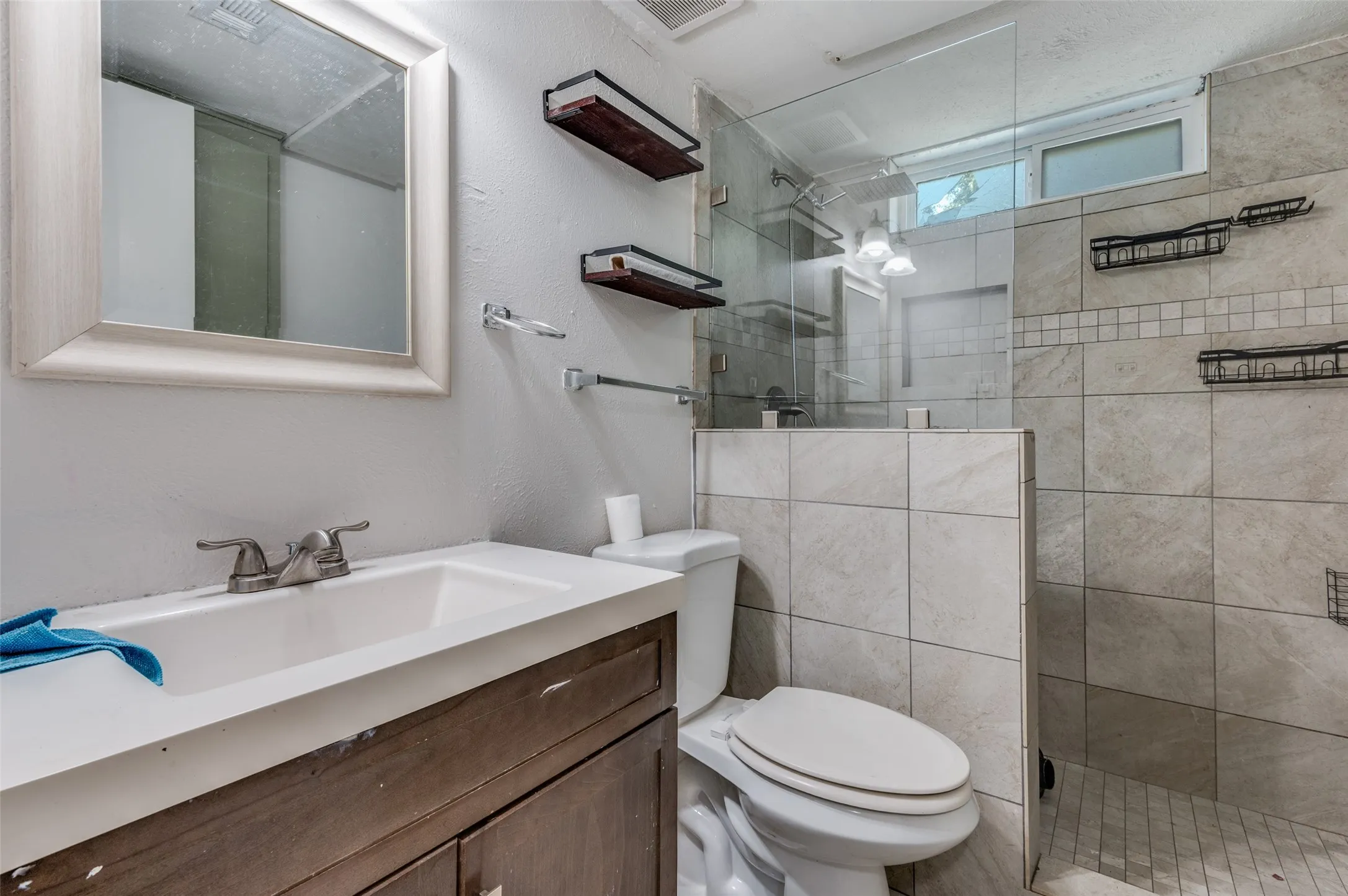 Vanity with integrated sink, framed mirror, and walk-in shower with glass enclosure and tiled walls