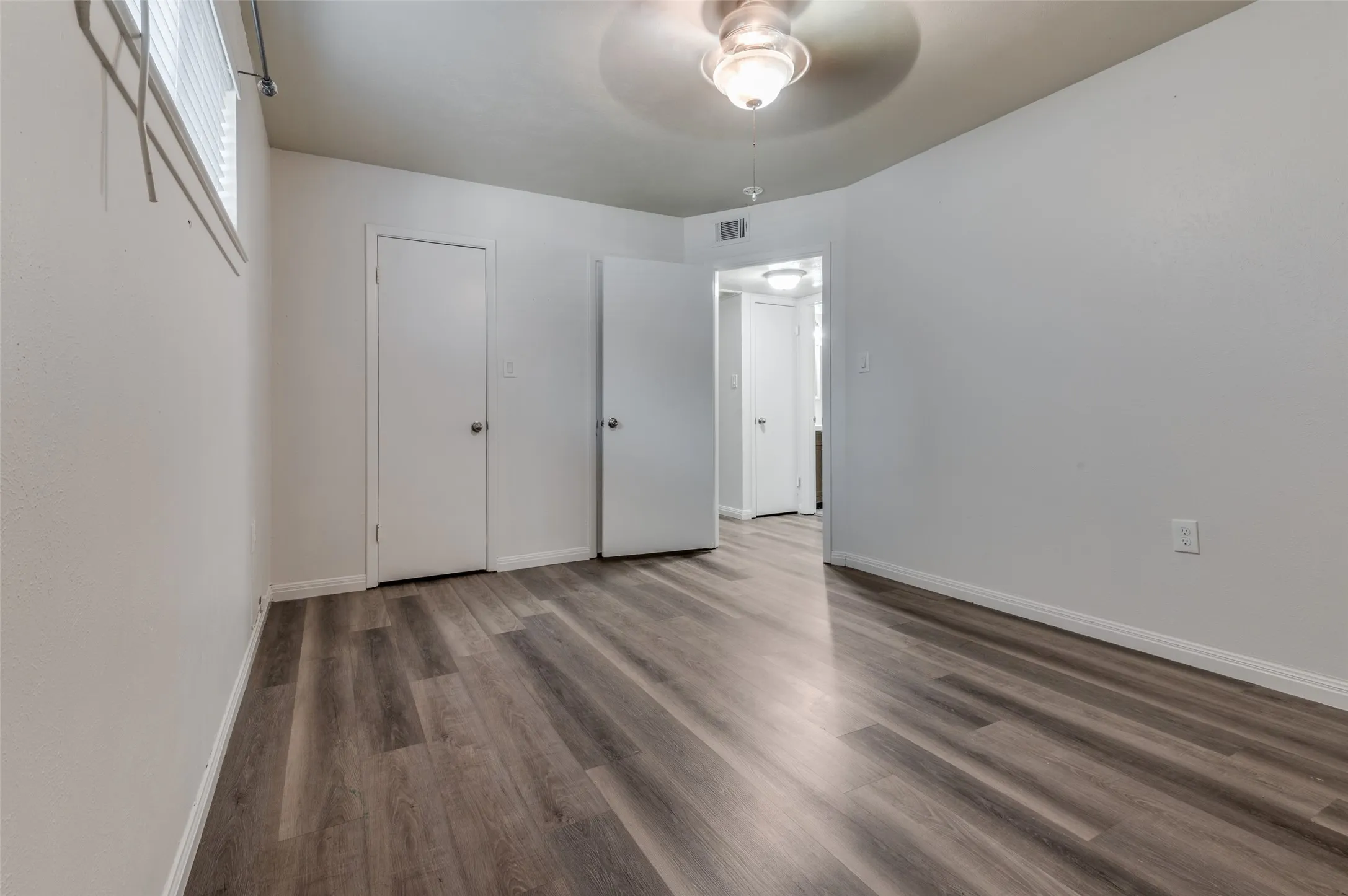 Wood-finish flooring throughout, white interior doors, and a ceiling fan with integrated lighting