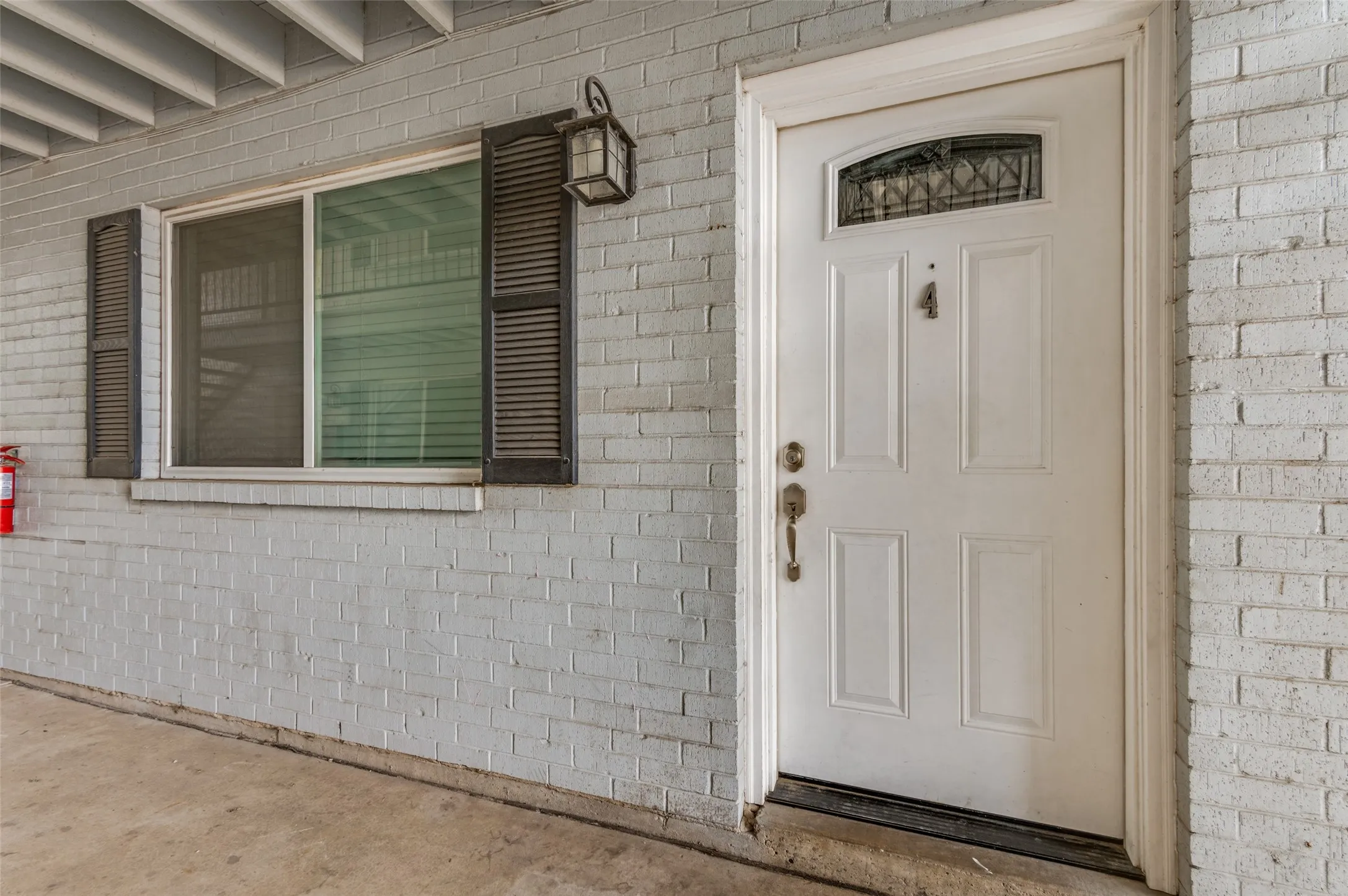 White brick exterior with a paneled entry door, transom window, and brass hardware