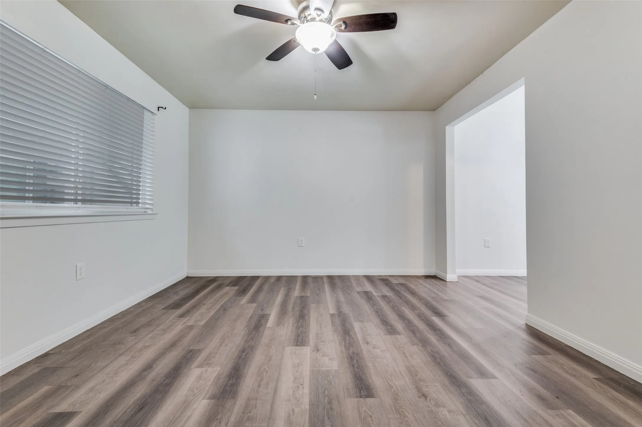 Wood-finish flooring, white walls, and a ceiling fan with integrated lighting