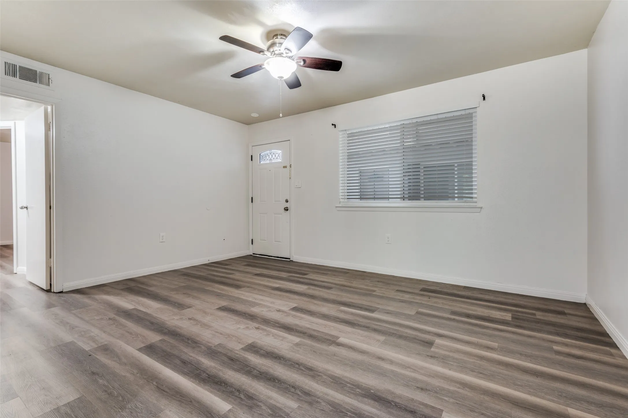 Wood-finish flooring throughout, white walls, ceiling fan with integrated lighting, and a window with blinds