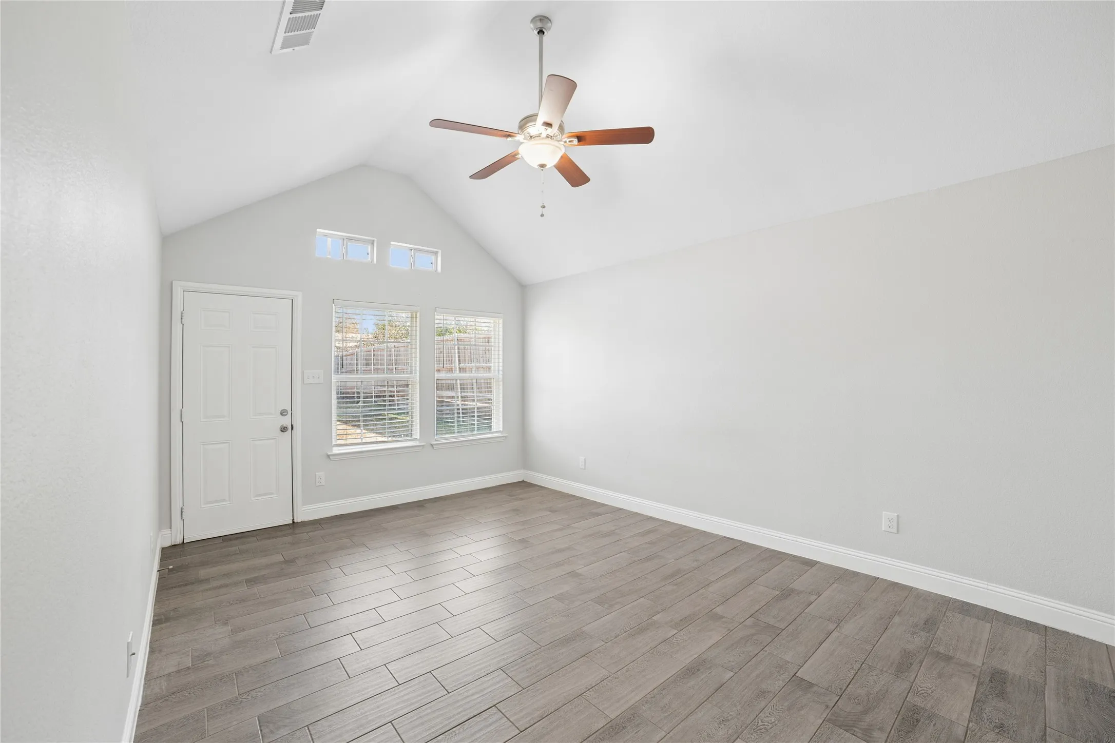 Vaulted ceiling with a ceiling fan, three transom windows, two large windows with blinds, and wood-finish flooring