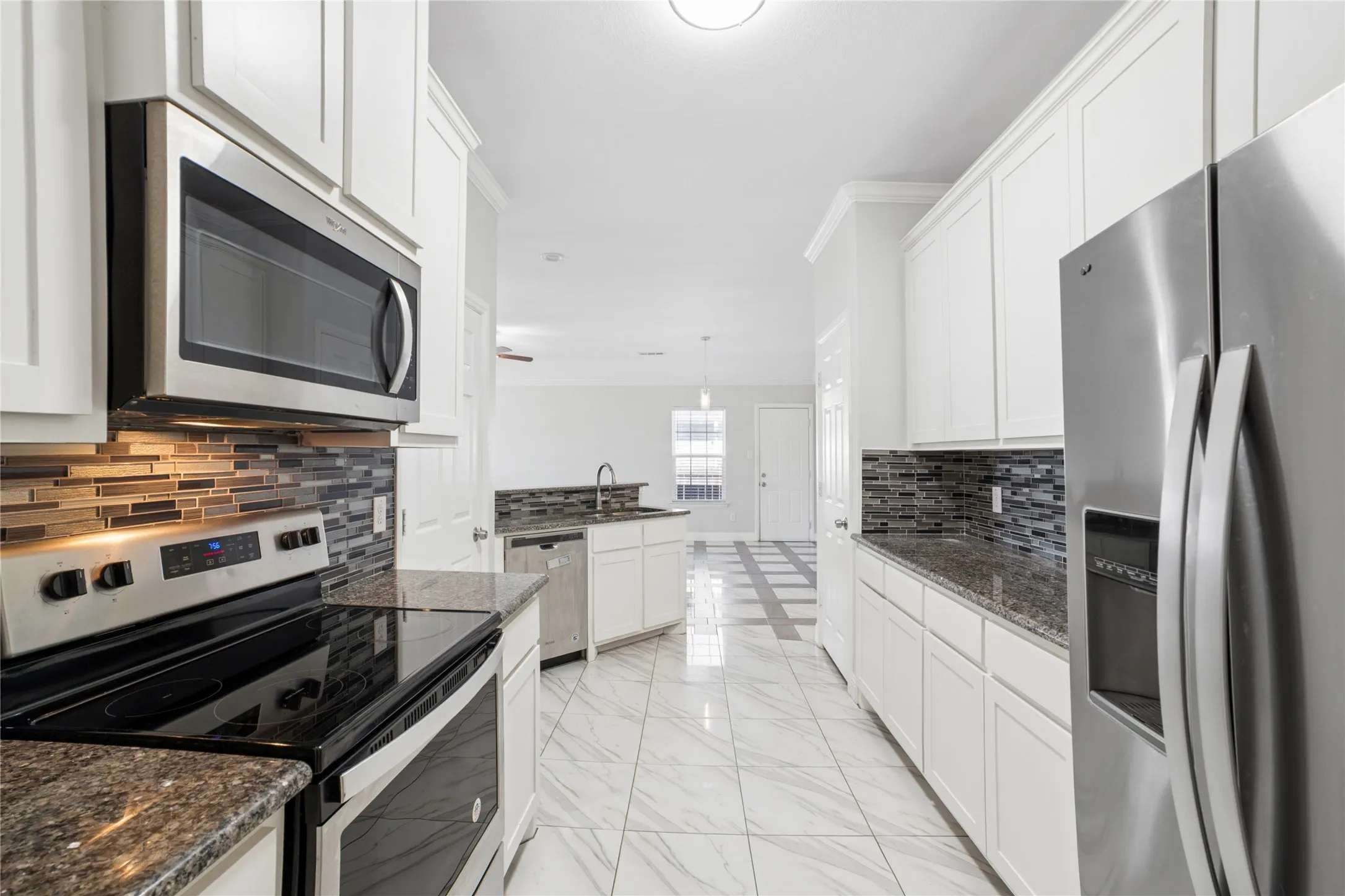 White cabinetry, stone countertops, stainless steel appliances, tile backsplash, and patterned tile flooring