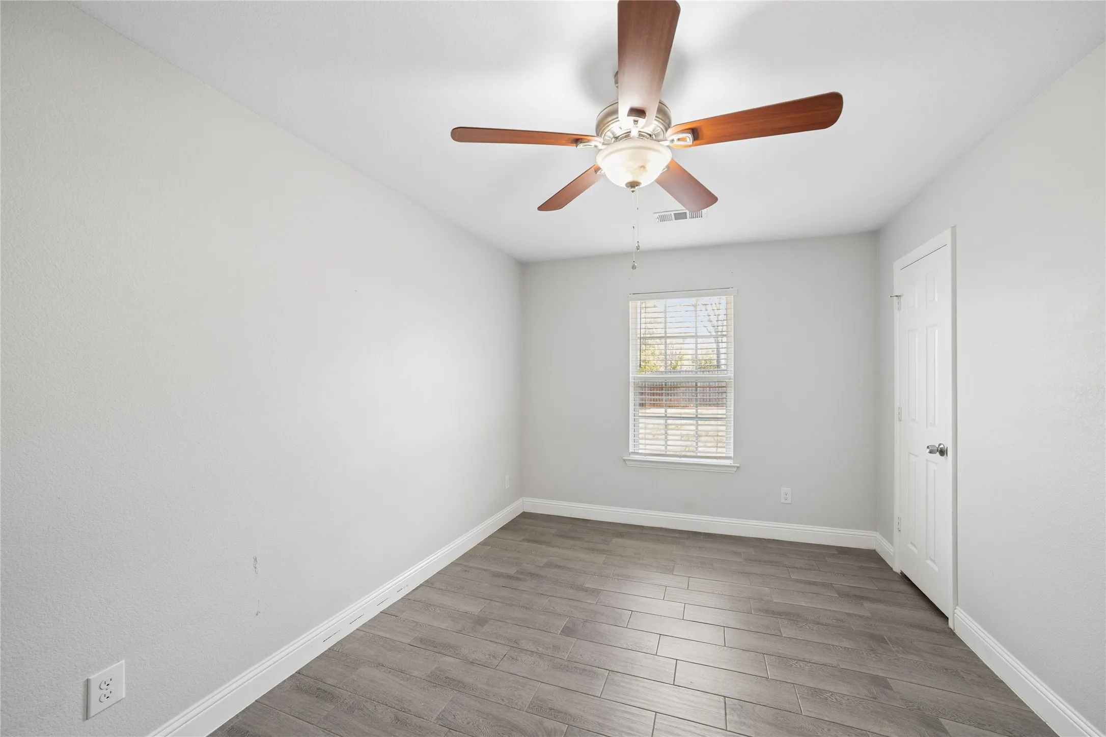 Wood-finish flooring, ceiling fan with light fixture, window with blinds, and white paneled door