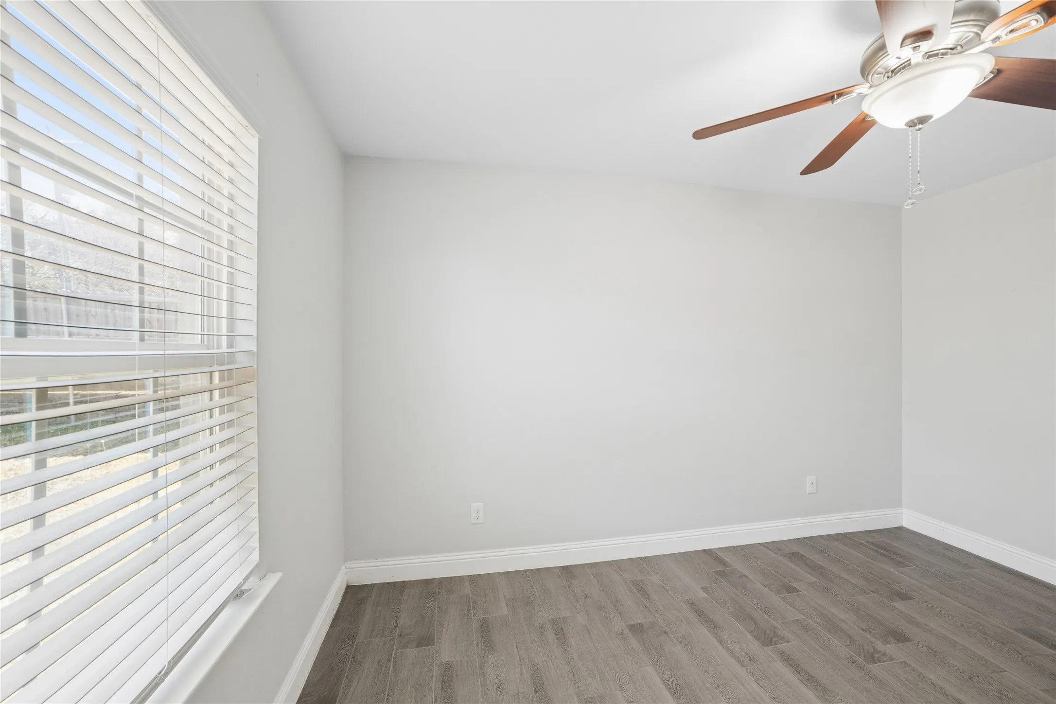 Bright, airy bedroom featuring plank-style wood-finish flooring, clean white walls, and ceiling fan with integrated lighting