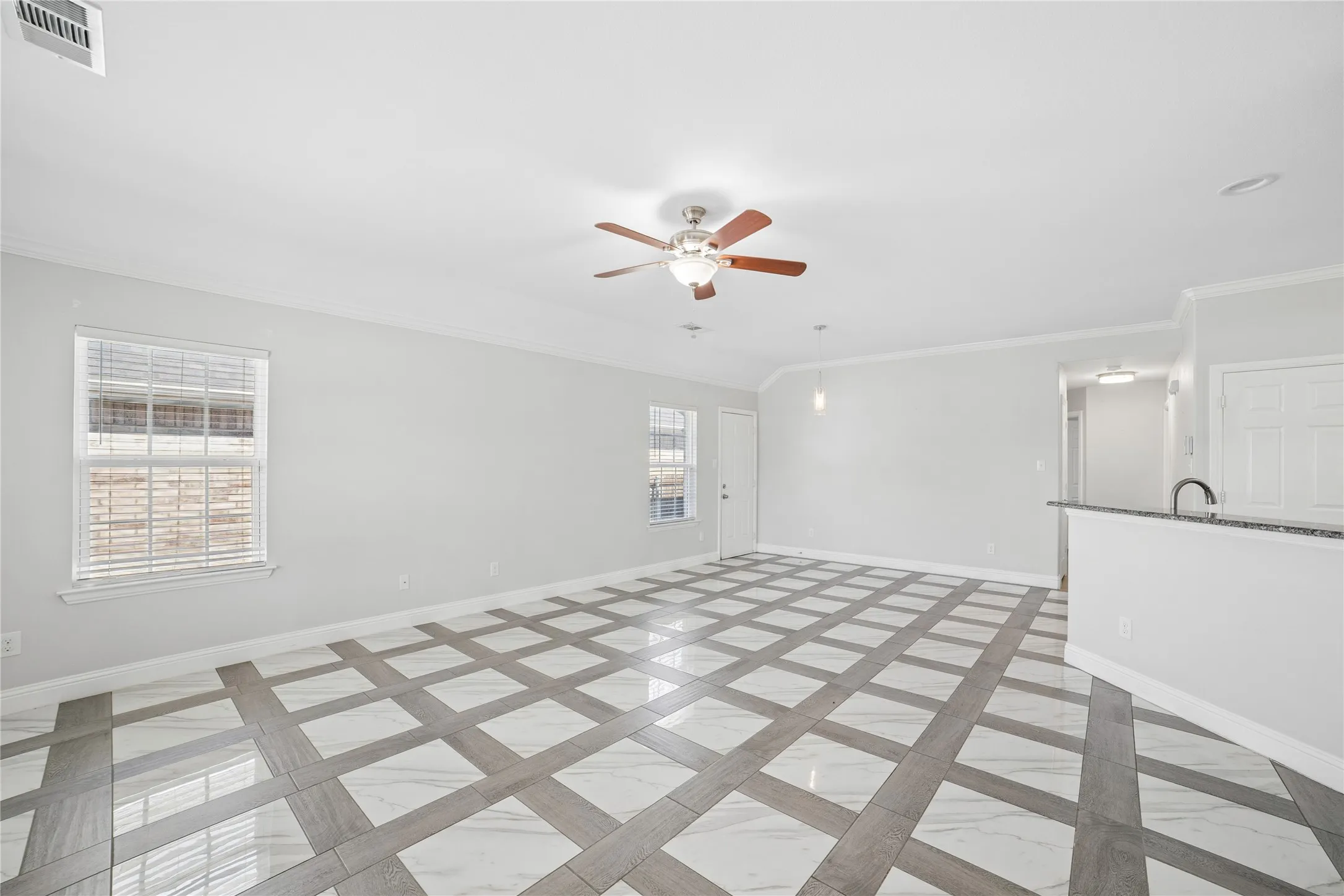 Spacious room featuring patterned tile flooring, a ceiling fan with integrated lighting, multiple windows, and crown molding