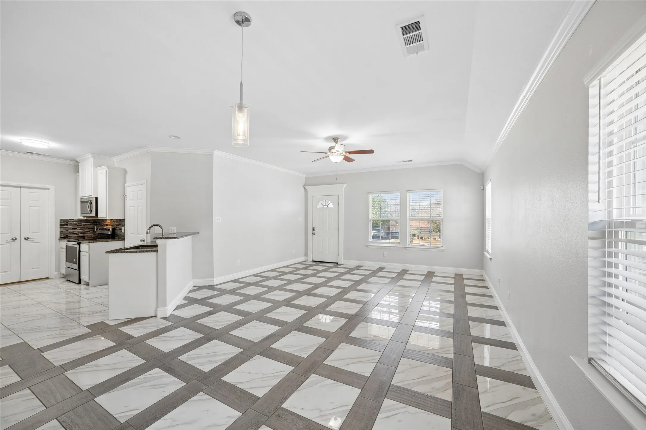 Vaulted ceiling with crown molding, patterned tile flooring, kitchen with dark countertops and white cabinetry, ceiling fan, and multiple windows
