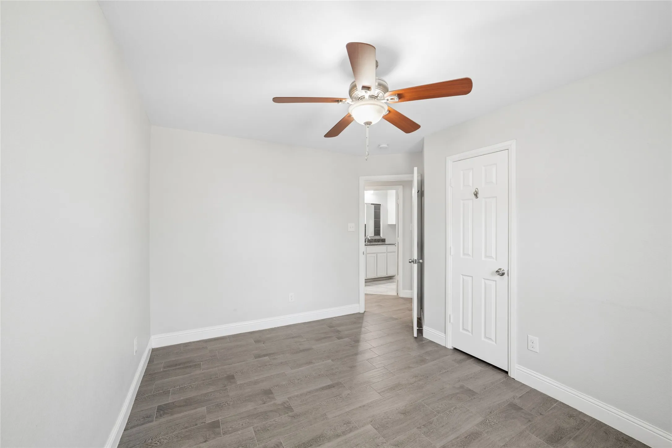Wood-finish flooring, white walls, white paneled door, and a ceiling fan with integrated lighting