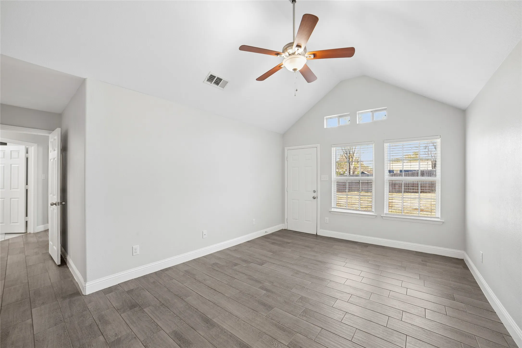 Vaulted ceiling featuring a ceiling fan, wood-finish flooring, multiple windows with blinds, and white trim