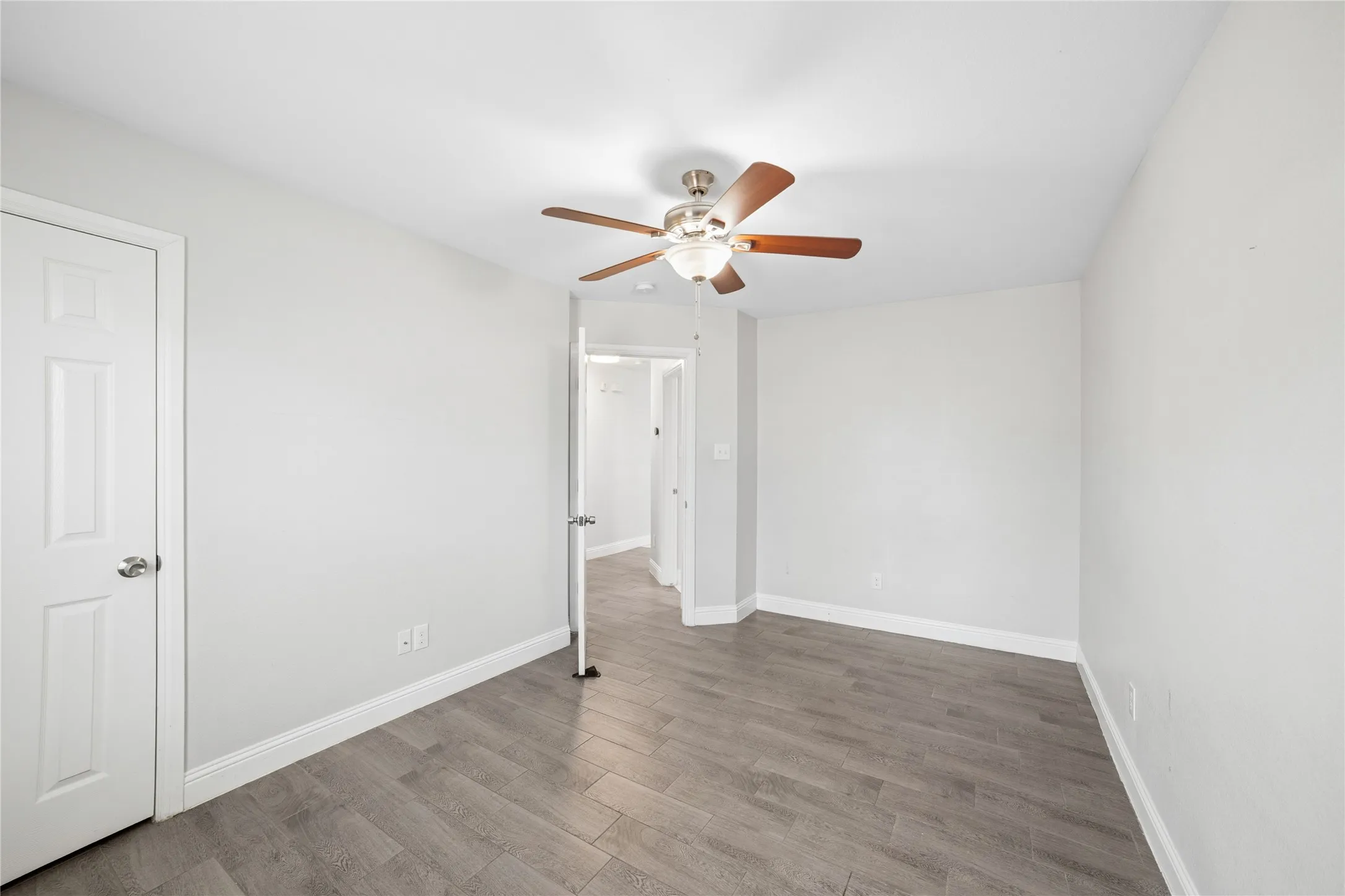 Recessed ceiling fan with wood-finish blades, light gray walls, wood-finish flooring, and white interior doors