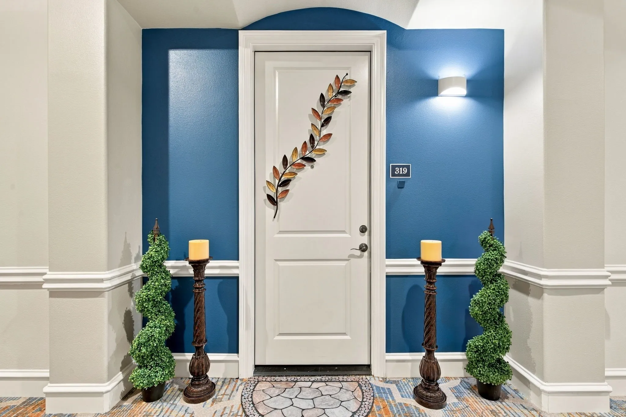 Entry door with white trim, a decorative arched alcove, and a contemporary wall sconce