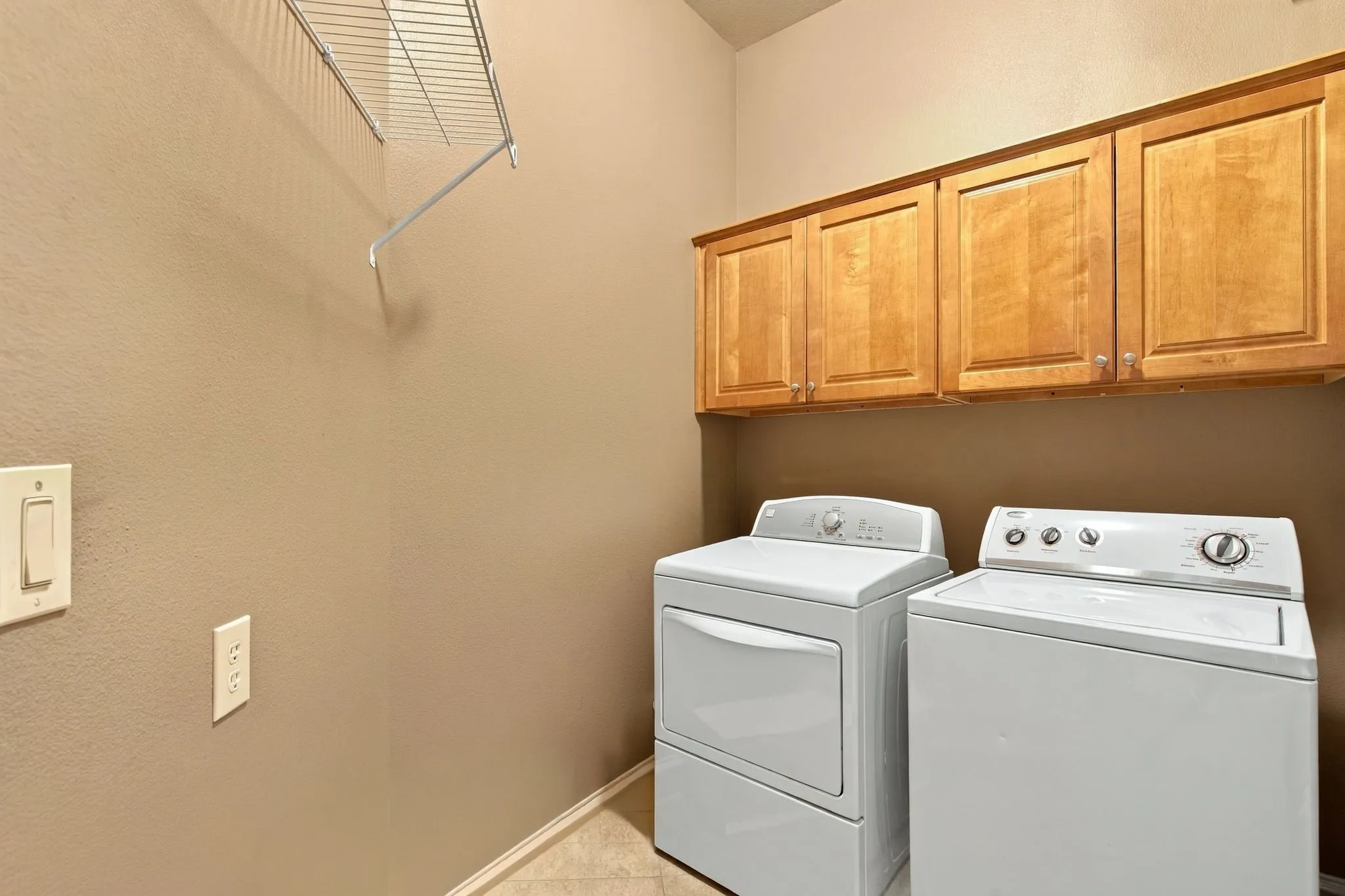 Wall-mounted shelving, overhead wood cabinetry, and tile flooring