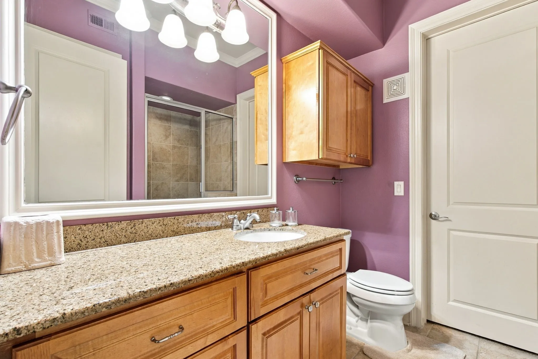 Light wood-finish vanity with a built-in sink, granite countertop, and matching overhead cabinetry