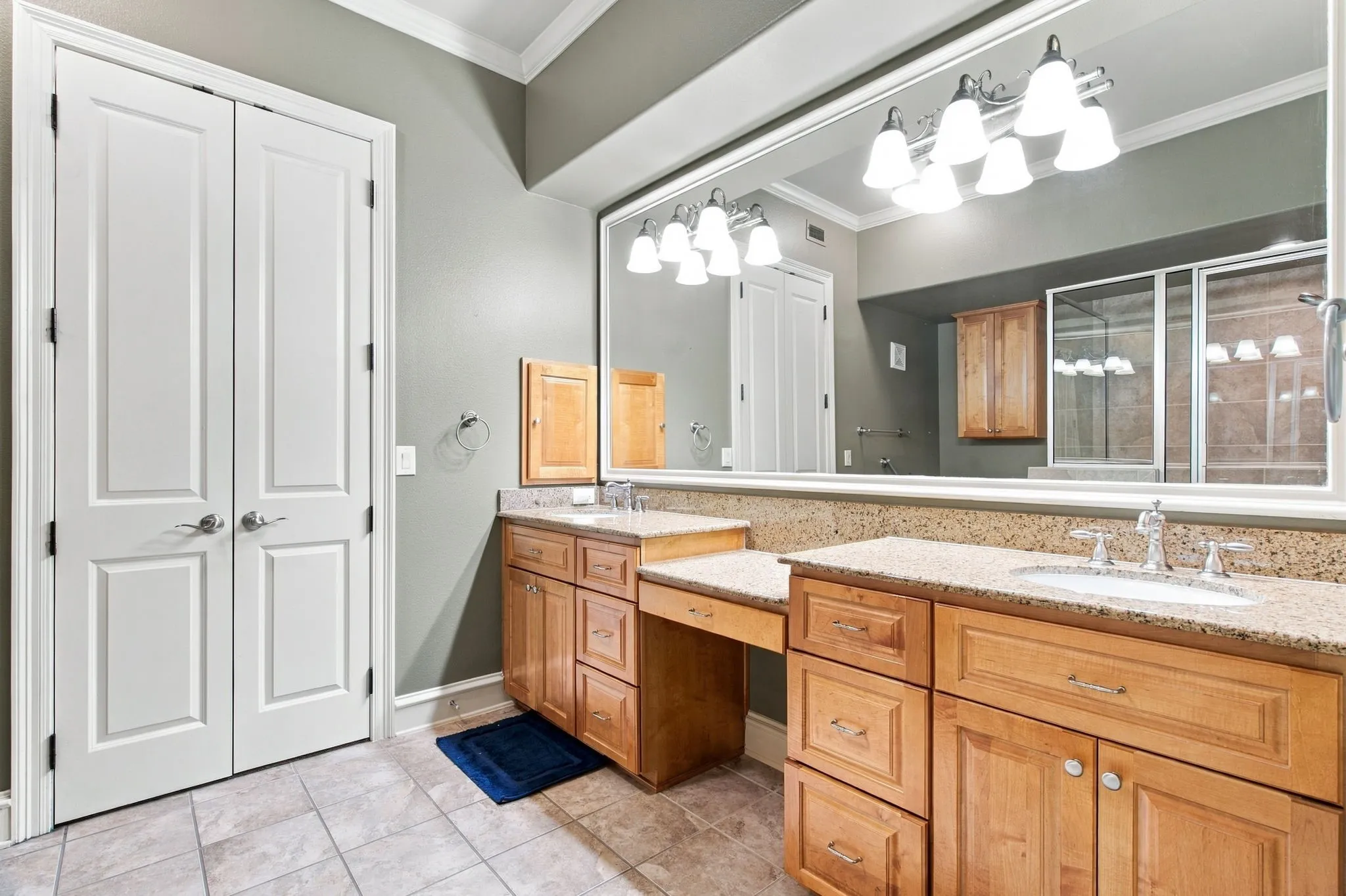 Dual vanities with stone countertops, integrated sink, large wall mirror, and wood cabinetry