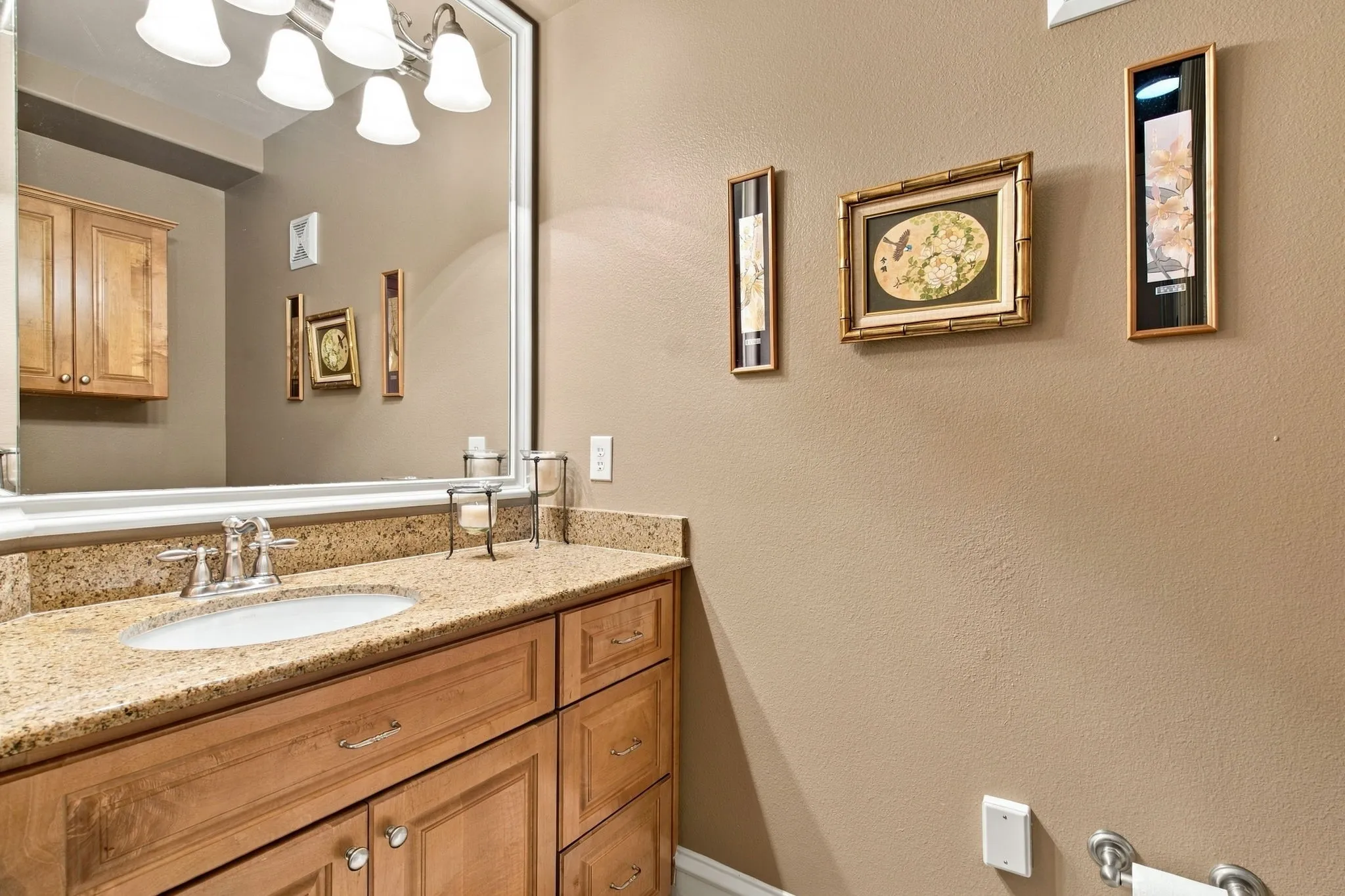 Elegant bathroom vanity featuring warm wood cabinetry, granite countertop, and a large framed mirror with integrated lighting