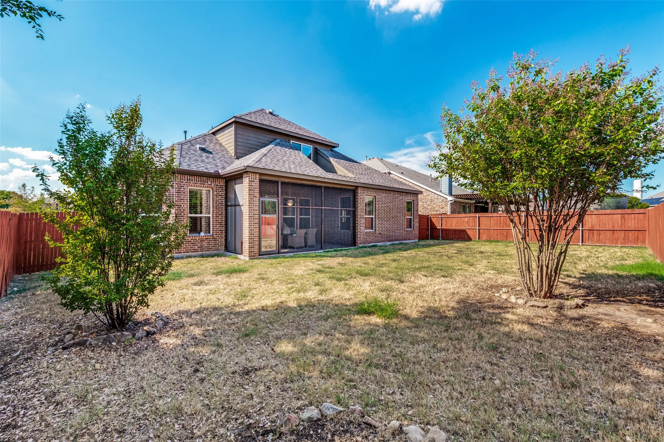 Brick exterior with a screened patio, shingled roof, and a wood privacy fence