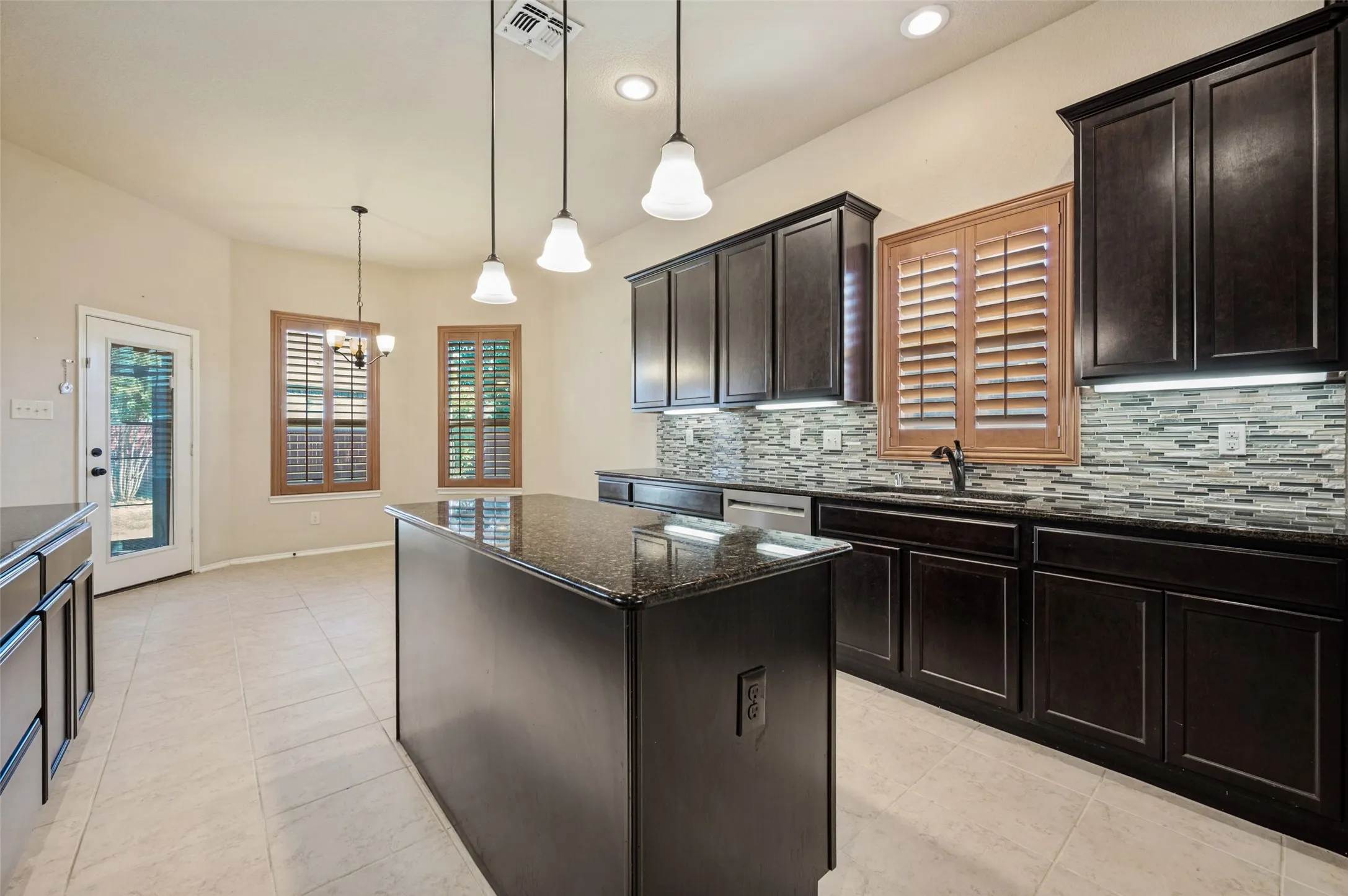 Spacious kitchen featuring dark wood cabinetry, a central island with a granite-style countertop, and a tiled backsplash