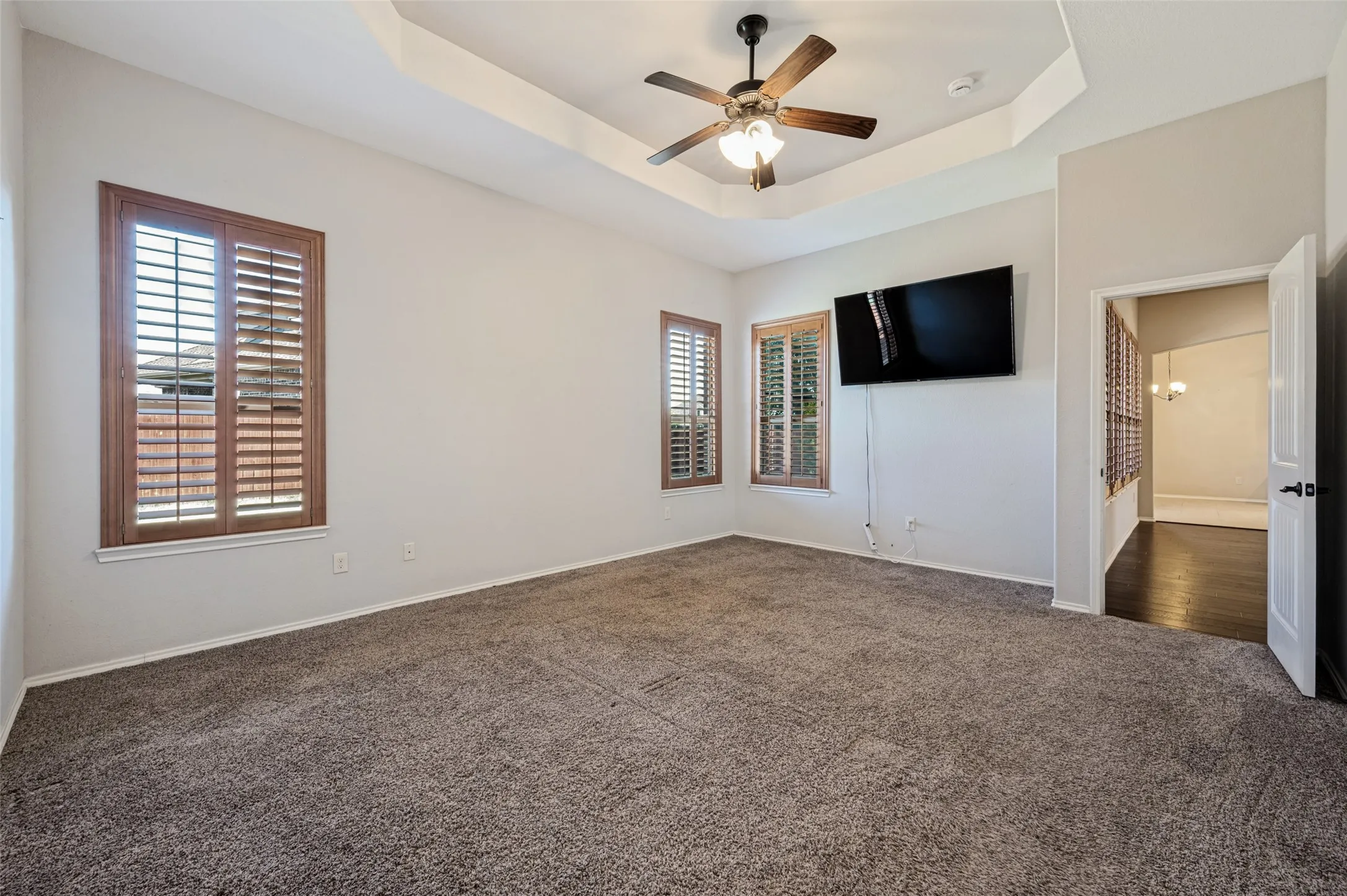 Tray ceiling with a ceiling fan, two windows with wood-finish shutters, and wall-to-wall carpeting