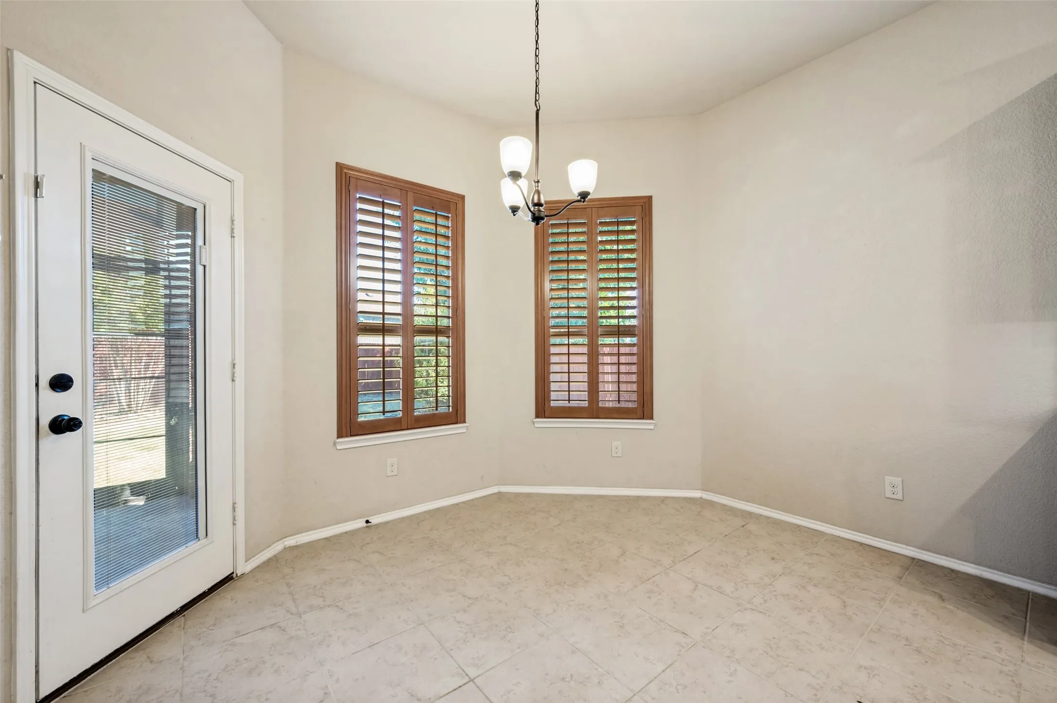 Tiled flooring, two windows with wood-finish plantation shutters, ceiling-mounted light fixture, and a glass-paneled door