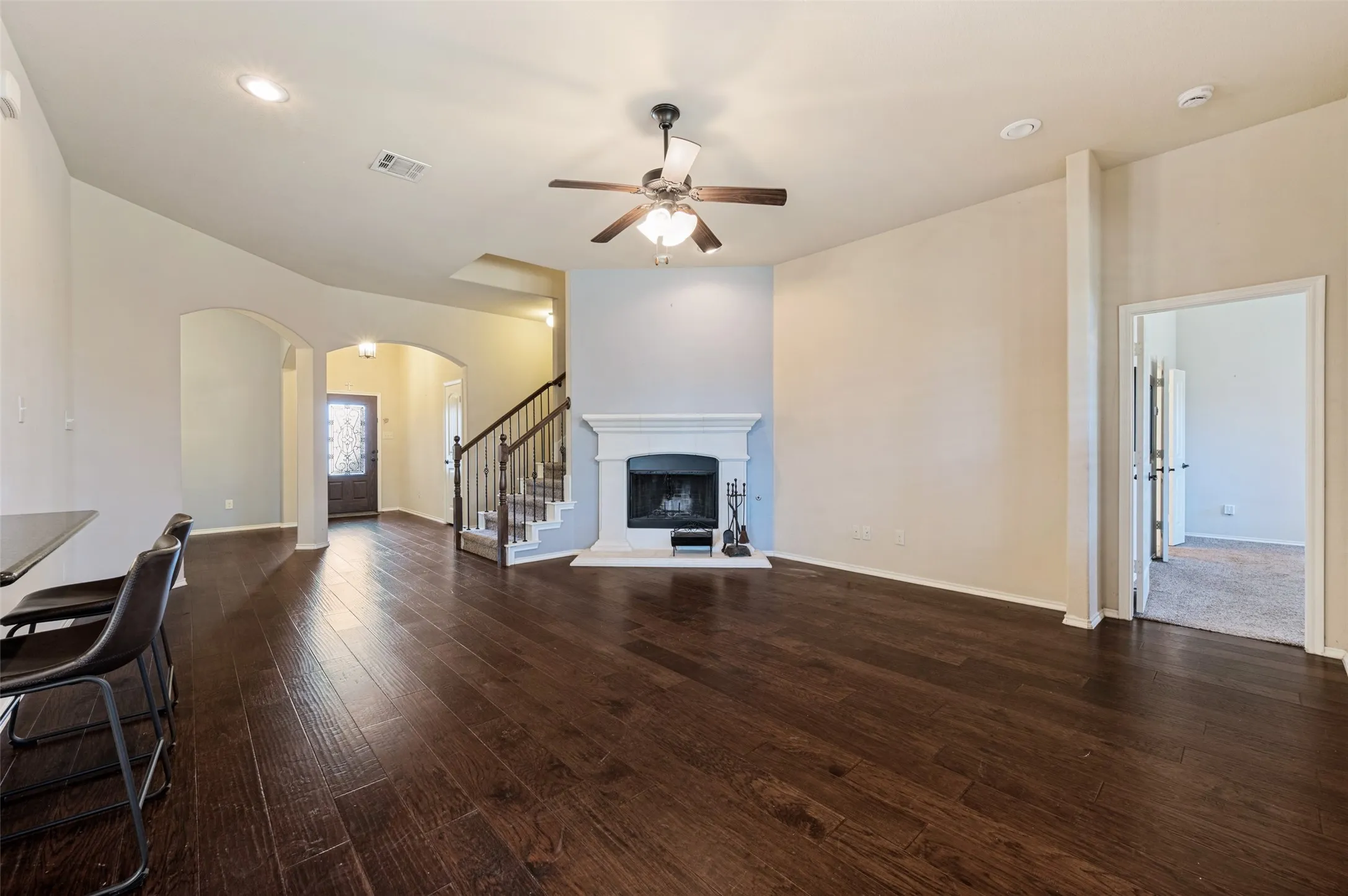 Wood-finish flooring throughout, a white fireplace with a mantel, a ceiling fan with integrated lighting, recessed lighting, and an arched entry