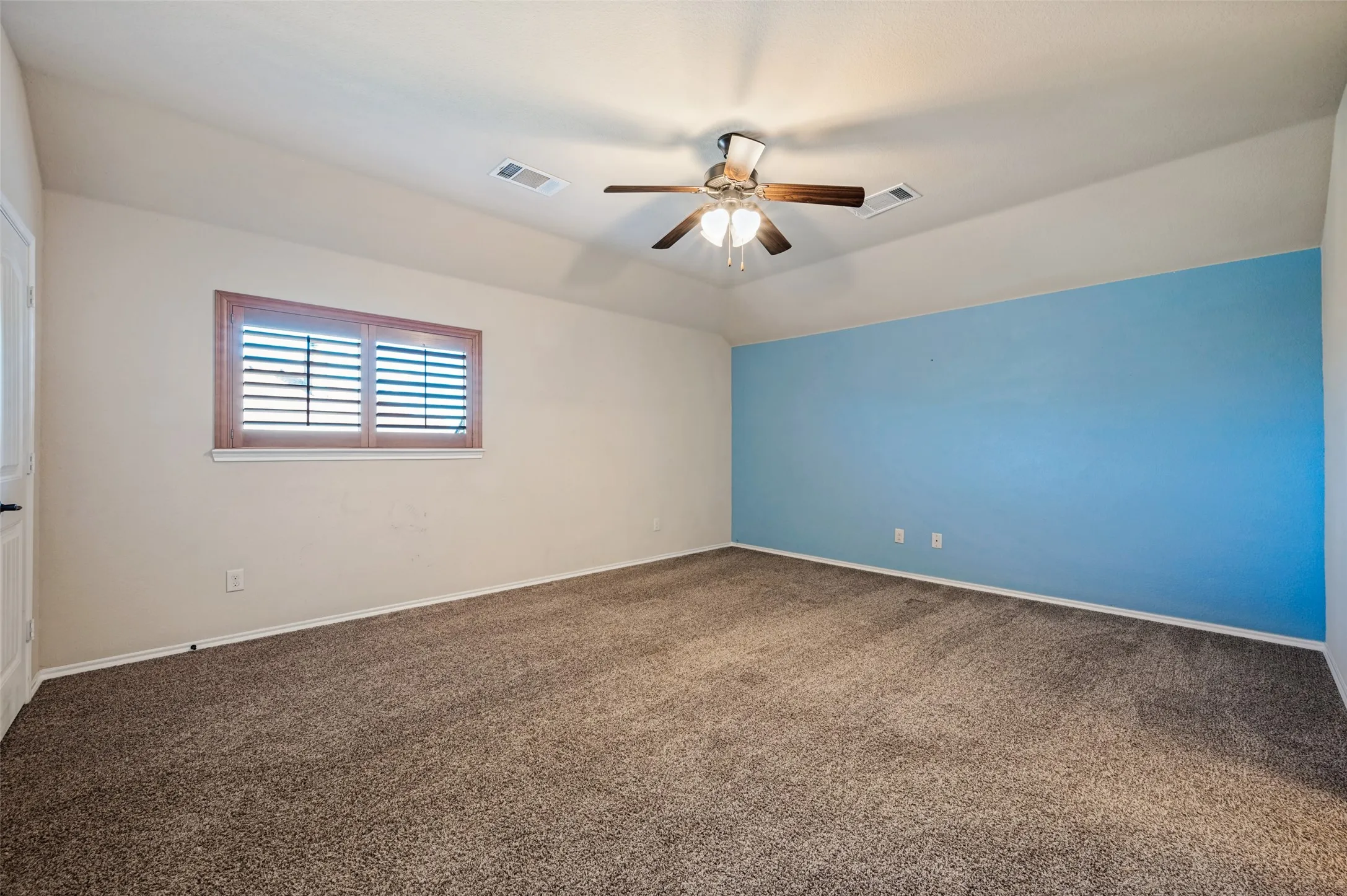 Carpeted room featuring a ceiling fan with light, a window with horizontal blinds, and a distinctive accent wall