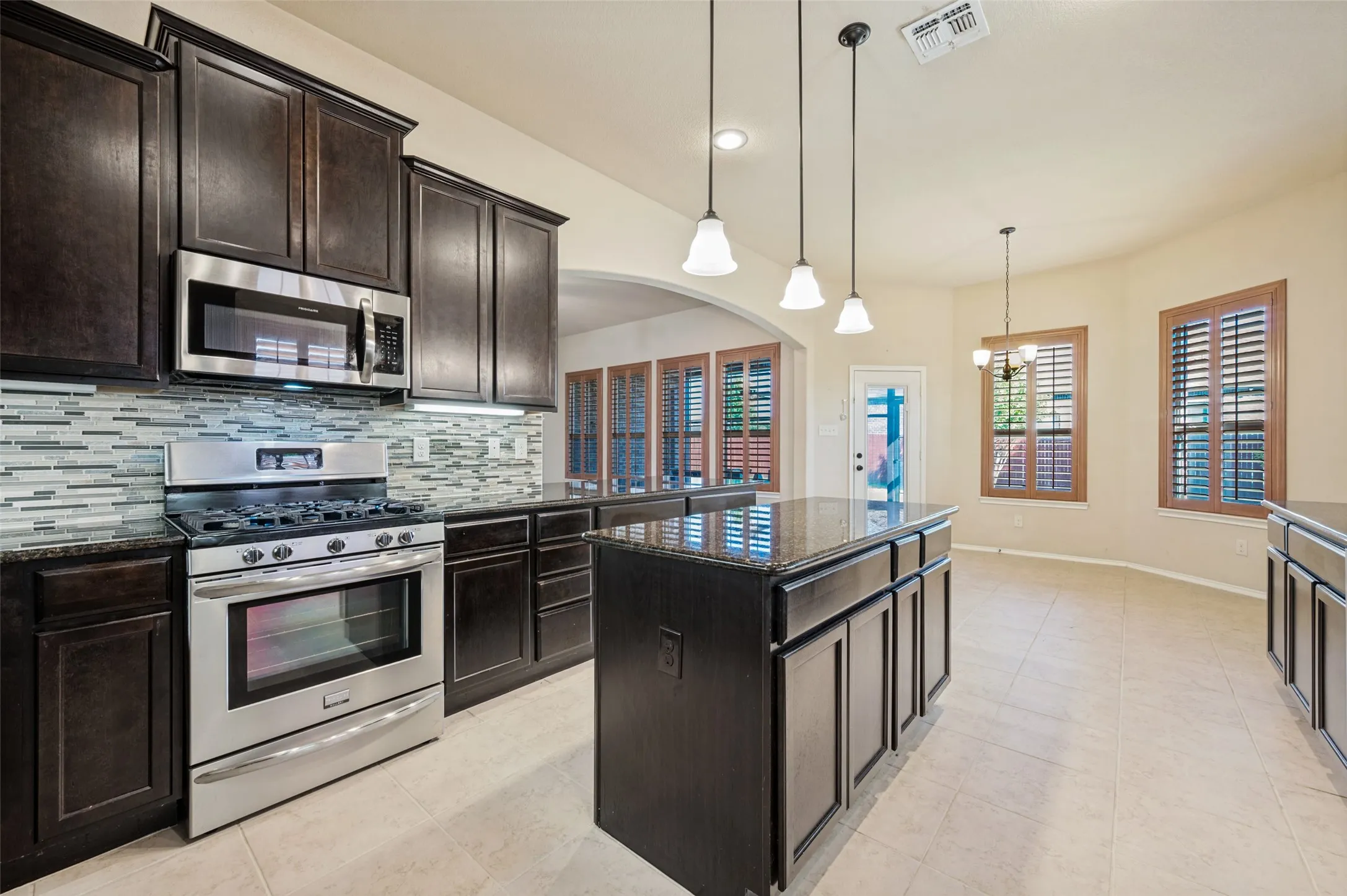 Kitchen featuring dark wood cabinetry, stainless steel appliances, a mosaic tile backsplash, and a central island with a stone countertop