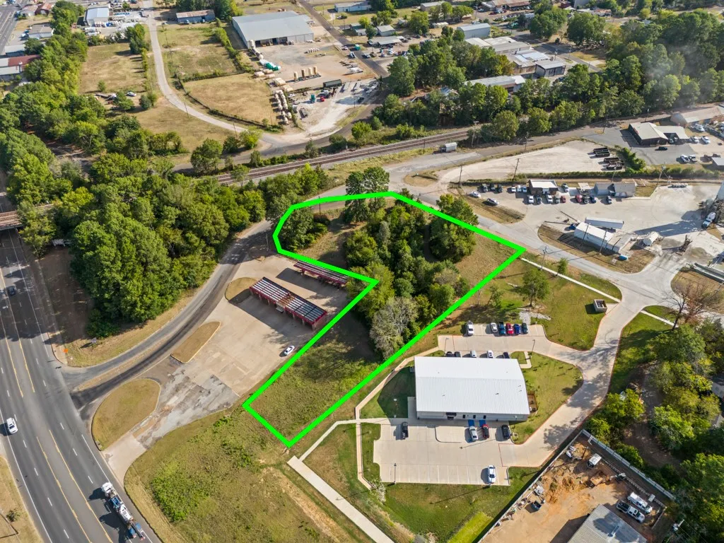 Aerial perspective of multiple parcels, including a developed commercial building, paved parking areas, and undeveloped land