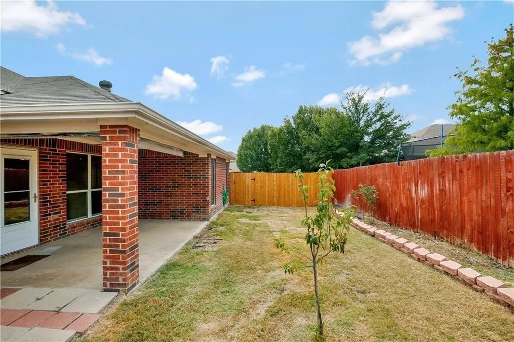Brick exterior with a covered patio, expansive lawn, and a wood privacy fence
