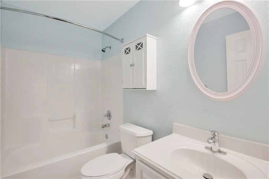 Spa-inspired bathroom featuring soft blue-gray walls, a white vanity with chrome fixtures, and a circular illuminated mirror